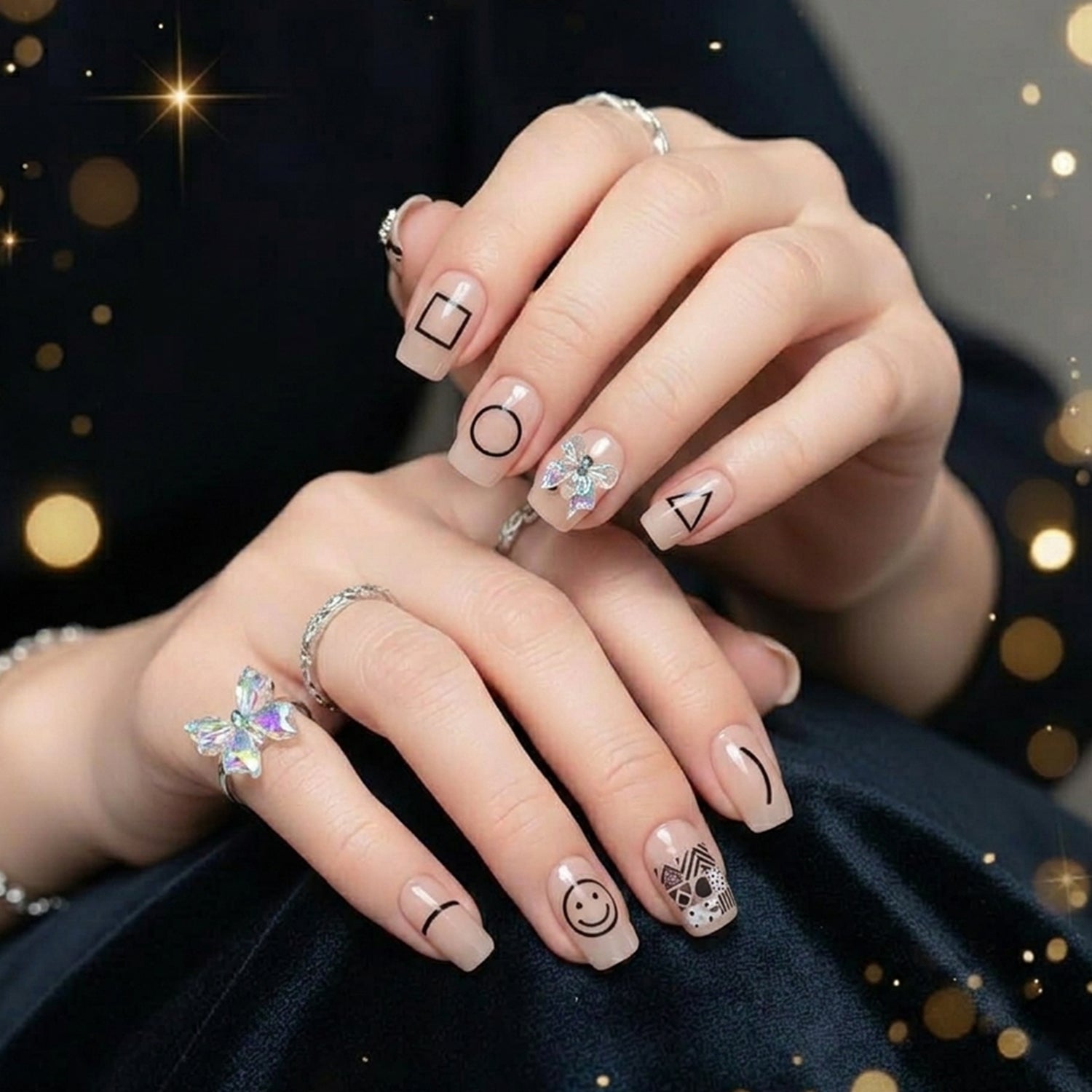 A person's hands wearing nude press-on nails with black geometric shapes, one with an iridescent bow, against a dark