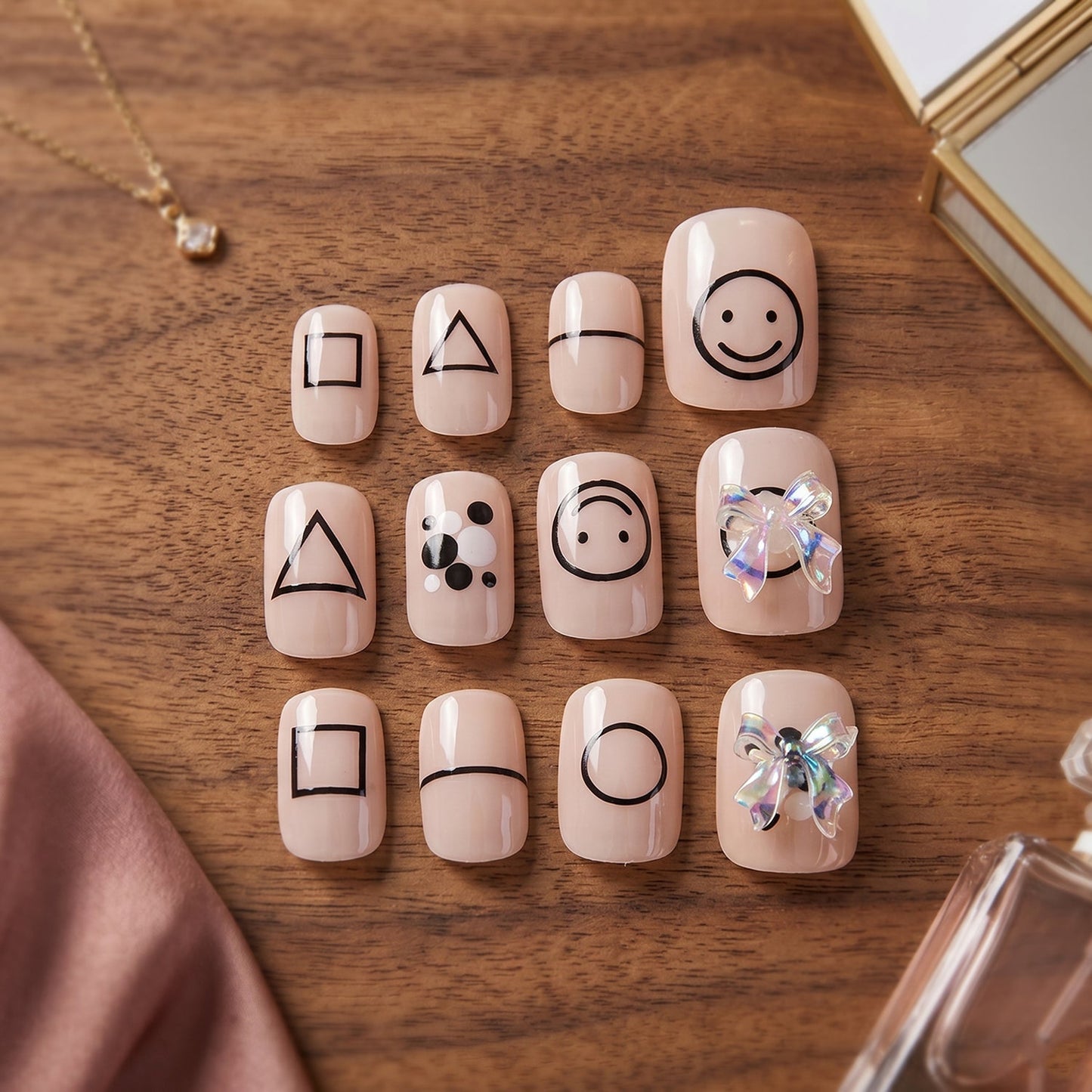 A set of 12 nude press-on nails with black geometric shapes and two iridescent bows, on a wooden surface with accessories.