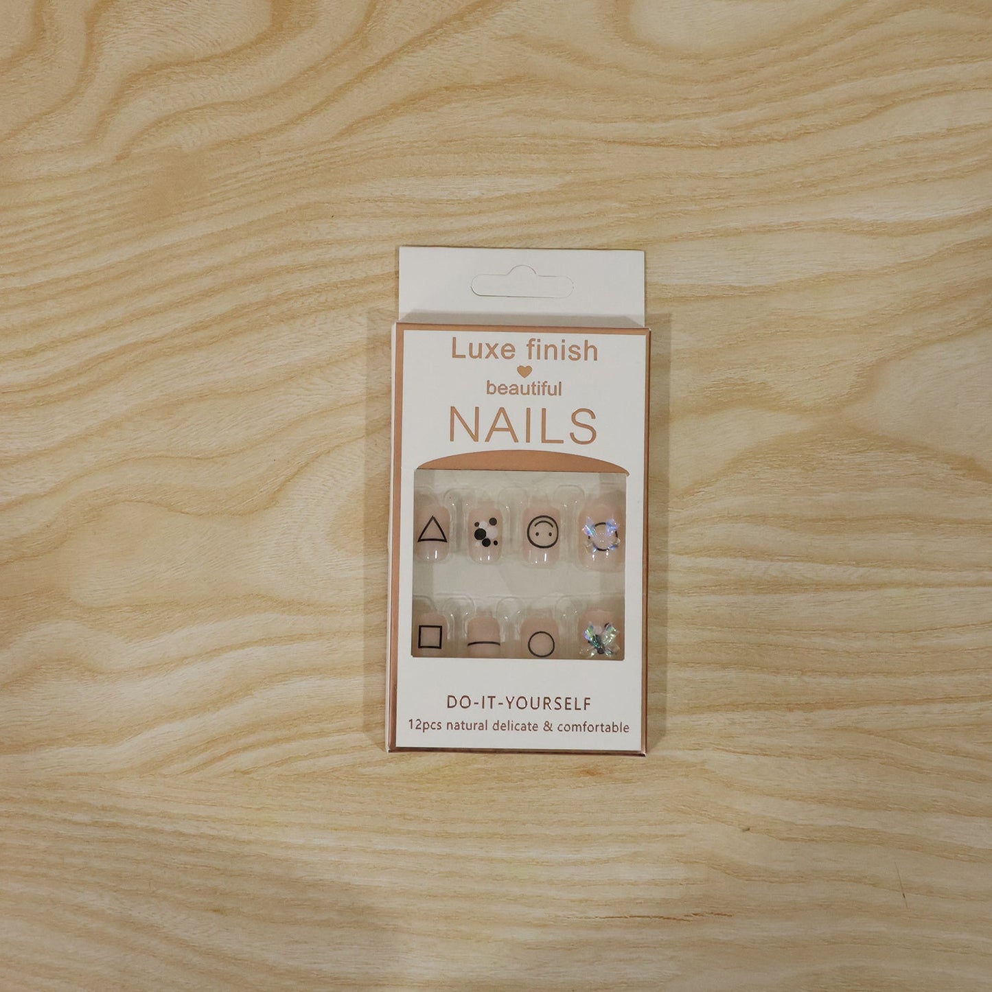 A white box of Luxe Finish Beautiful Nails, displaying 12 nude press-on nails with geometric designs and bows.