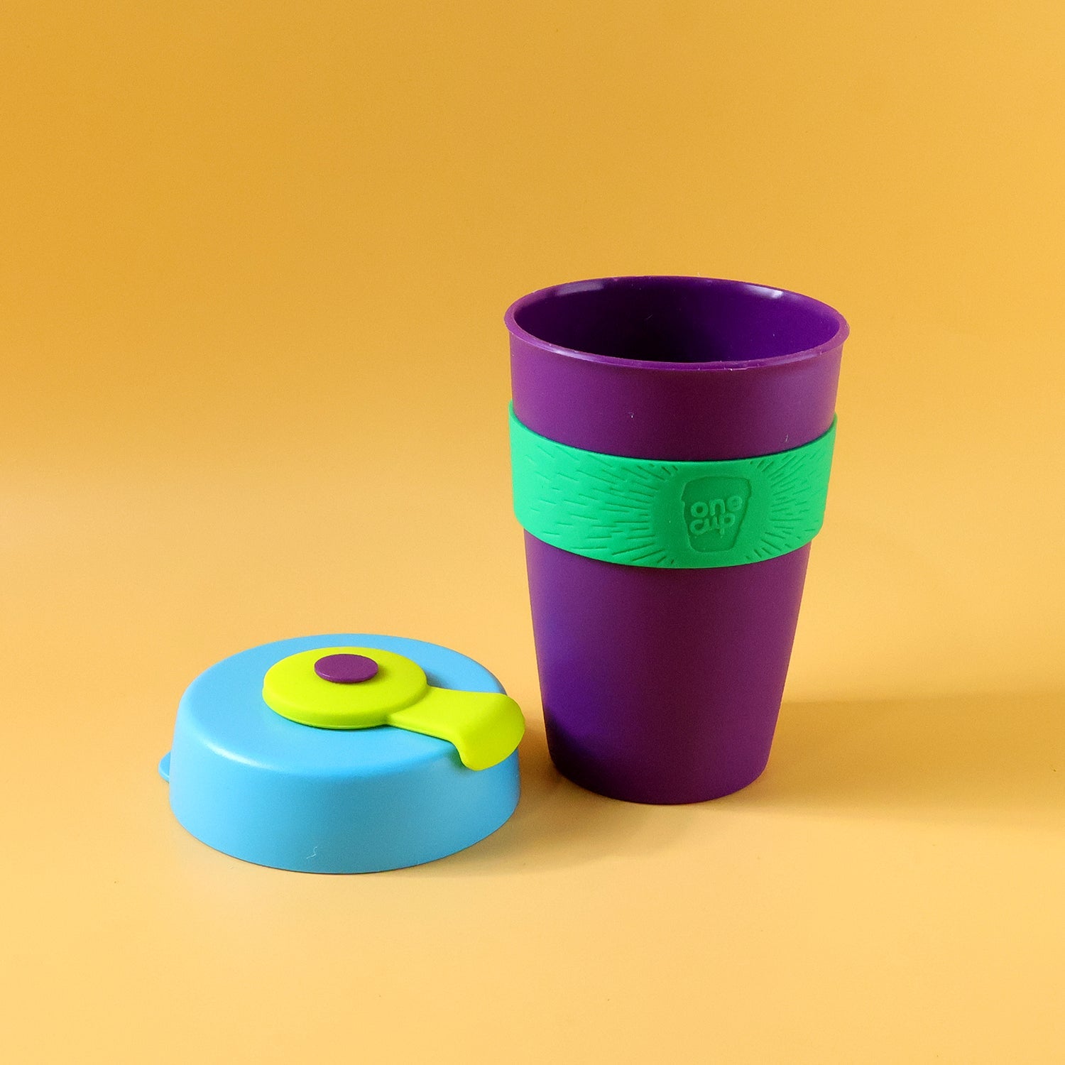 A purple cup with a green textured band and a detached blue lid with a green and purple stopper on a yellow background.