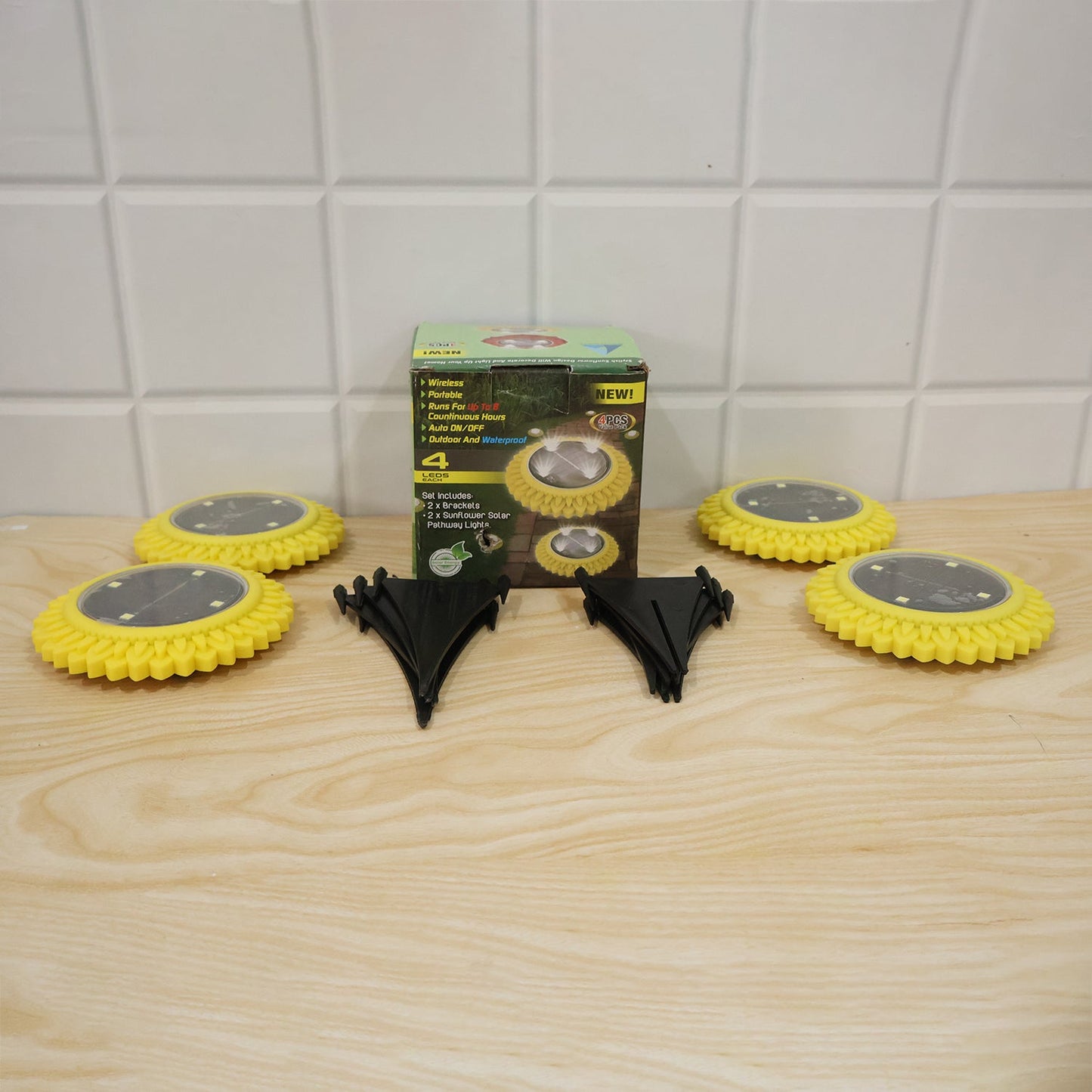 Four yellow solar lights, two black ground stakes, and a product box are arranged on a light wooden surface.