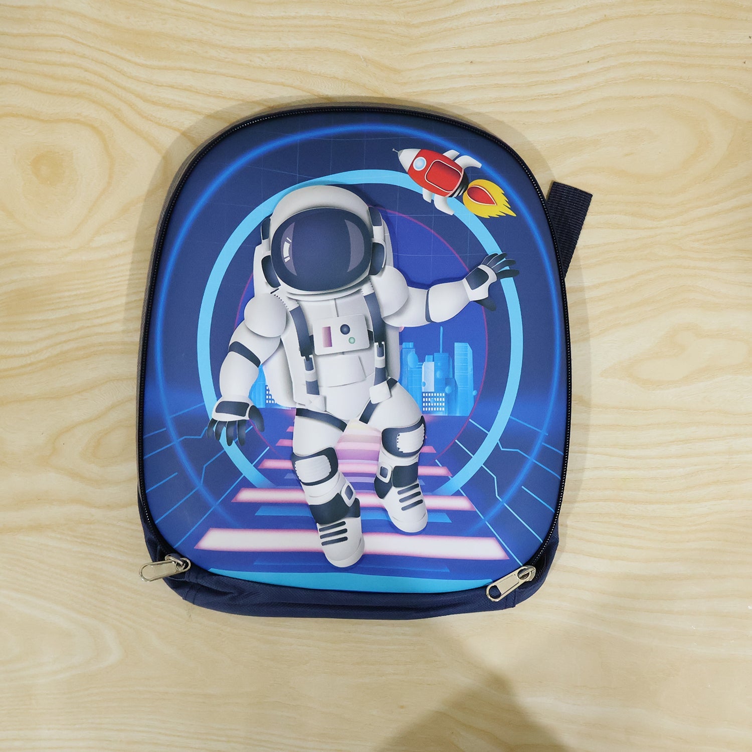 A navy blue hard-shell backpack with a white astronaut and rocket graphic is open, showing school supplies inside (1 Pc).