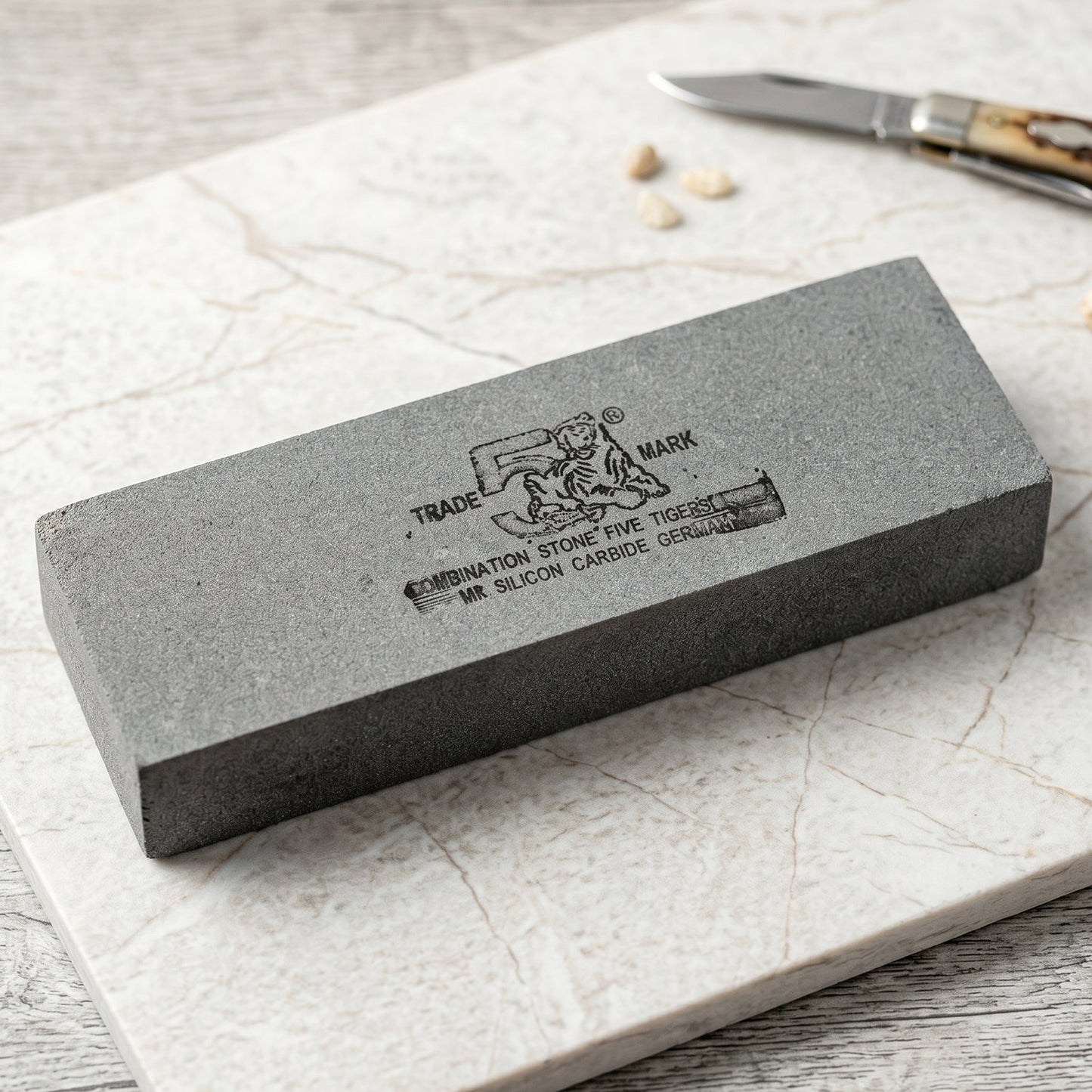 Gray rectangular sharpening stone with black text and tiger logo on a white marble surface next to a small knife.