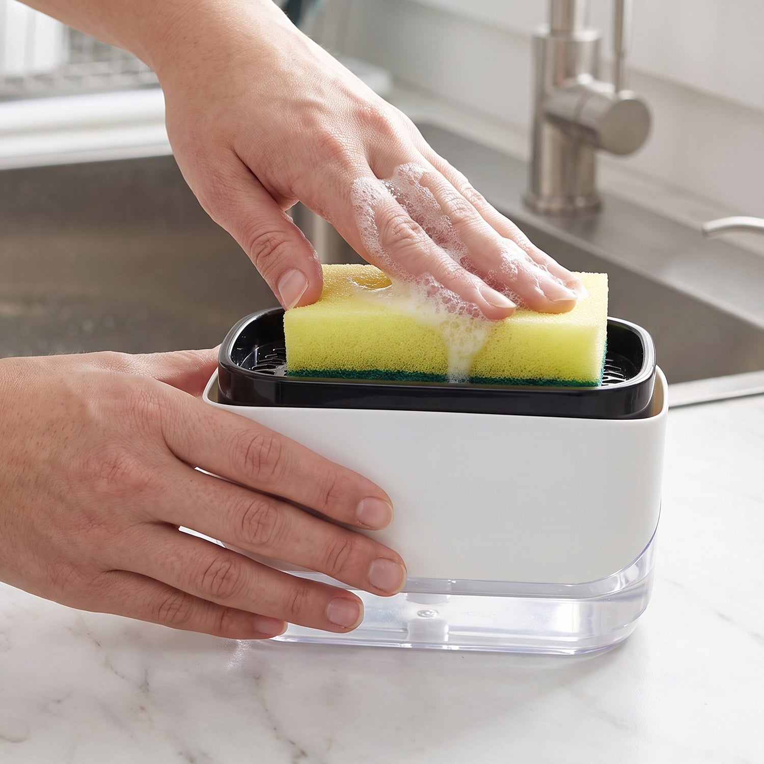 A person's hands press a yellow sponge onto a white and black soap dispenser, creating suds, next to a kitchen sink.