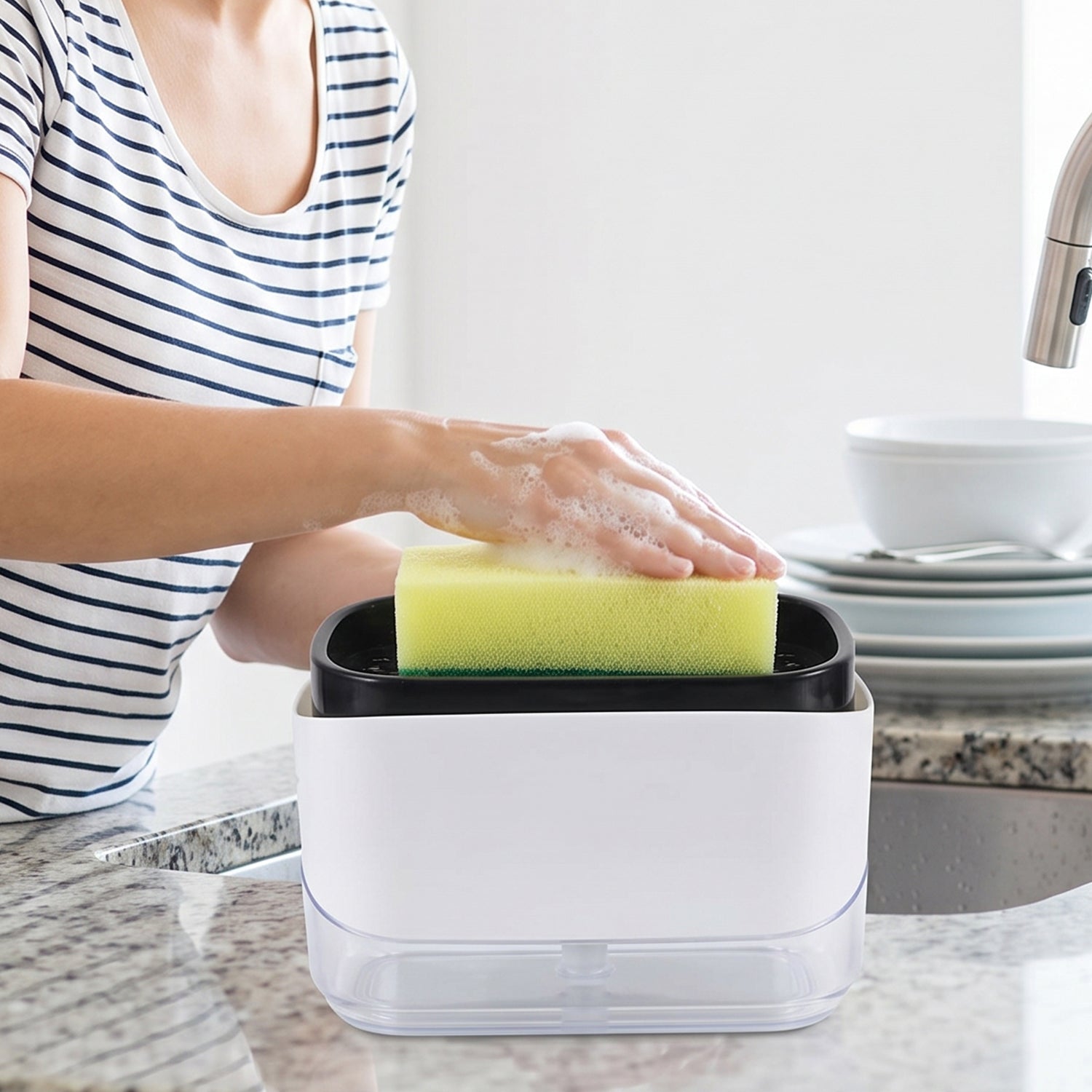 A person in a striped shirt presses a yellow sponge onto a white and black soap dispenser, creating suds, next to a sink
