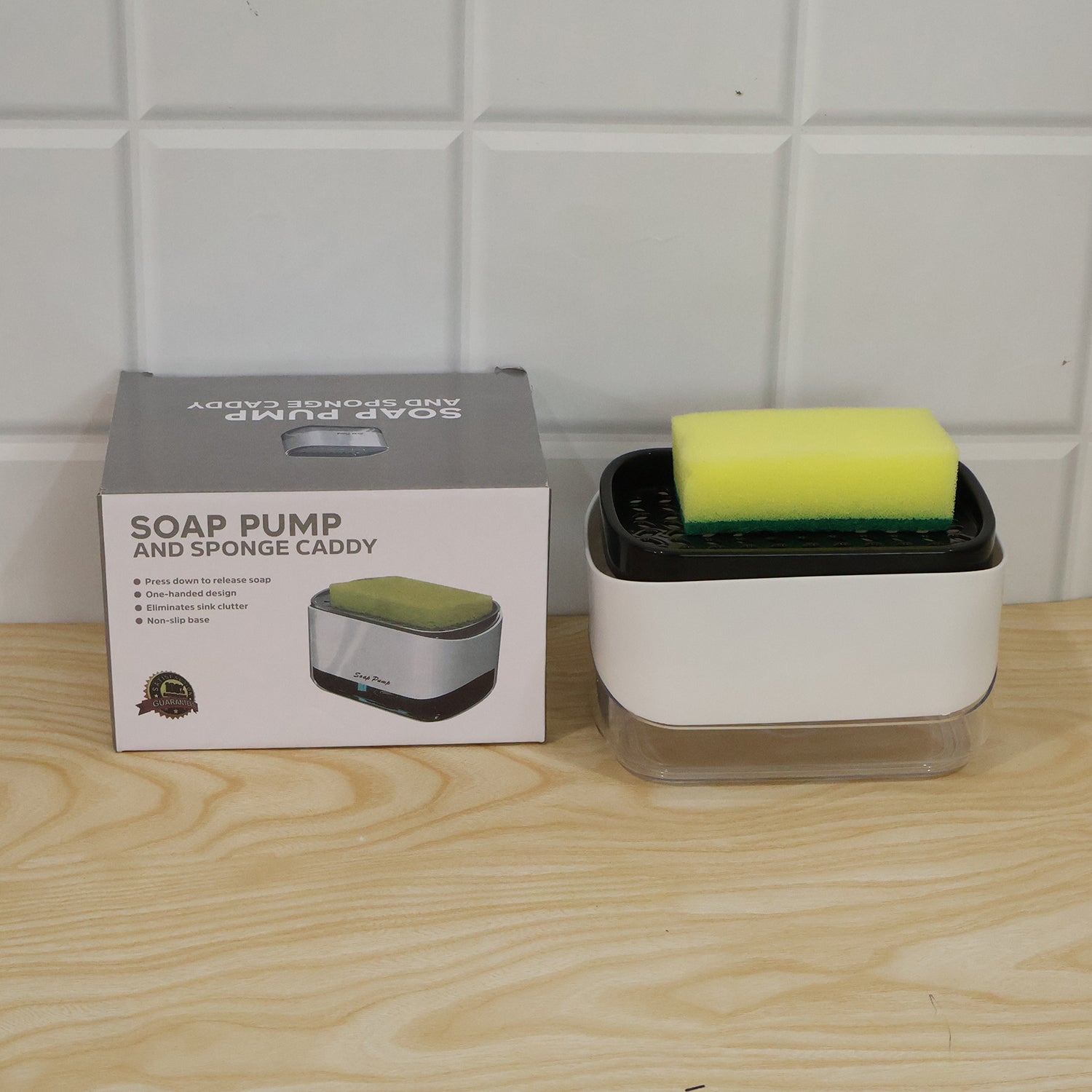A white and black soap dispenser with a yellow sponge sits next to its gray and white packaging box on a wooden surface.