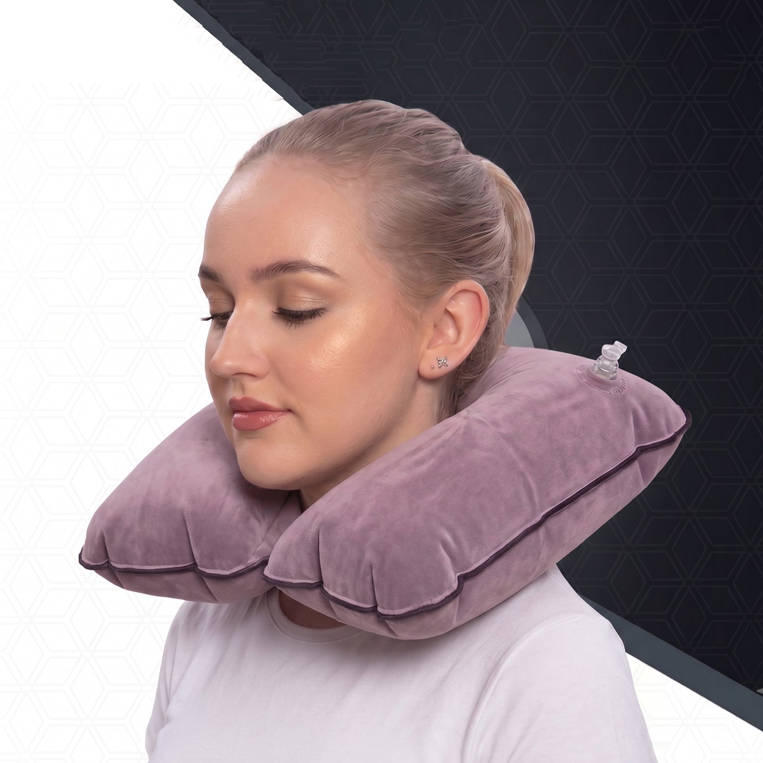 A woman wears an inflated purple velvet U-shape neck pillow, with a clear valve on the right, against a geometric background.