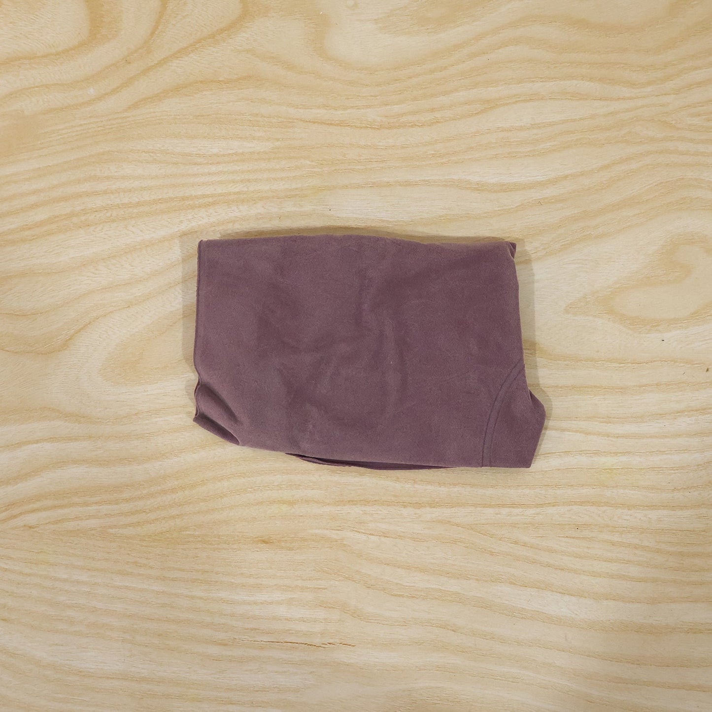 A deflated purple velvet U-shape neck pillow is folded neatly into a compact rectangle on a light wooden surface.