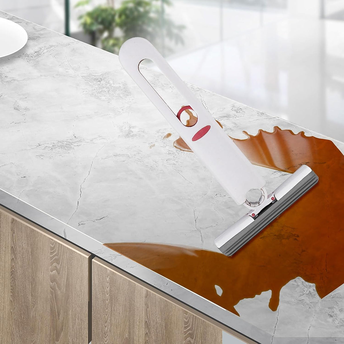 The white and red silicone squeegee is shown cleaning a brown liquid spill on a white marble countertop.