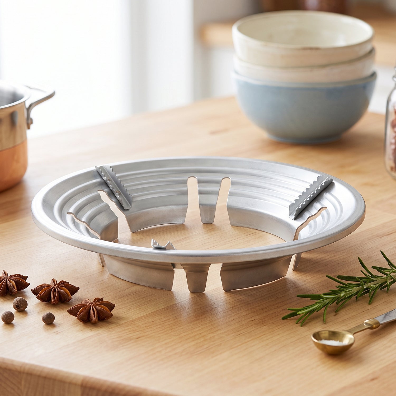 A silver gas stove trivet sits on a wooden counter next to star anise and rosemary sprigs.