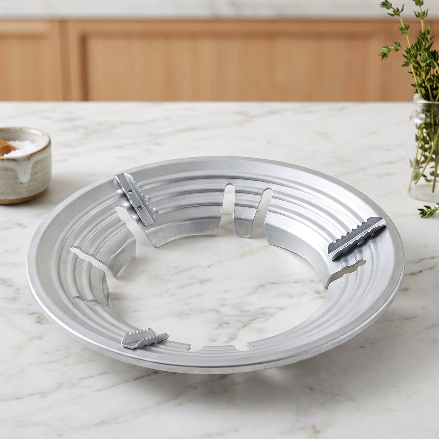 A silver gas stove trivet with a ribbed design rests on a white marble countertop.