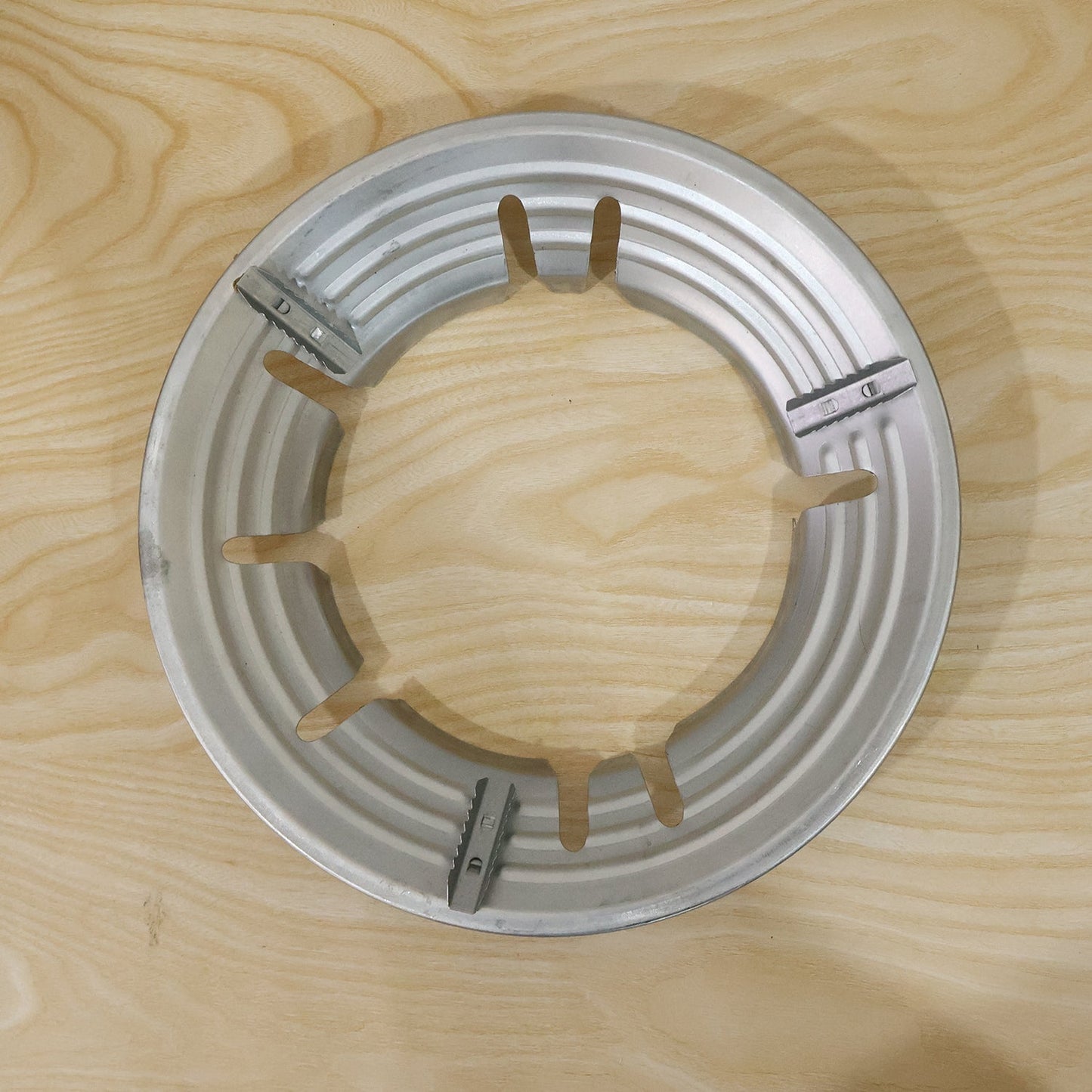 A top-down view of the silver gas stove trivet with a ribbed edge on a light wooden surface.