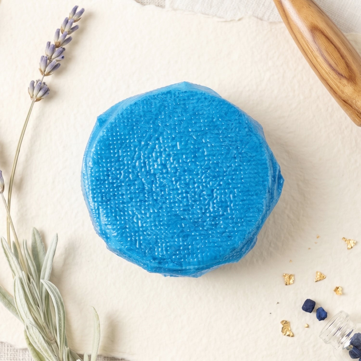 A blue toilet cleaner tablet on a textured white surface, with lavender and a wooden tool nearby.