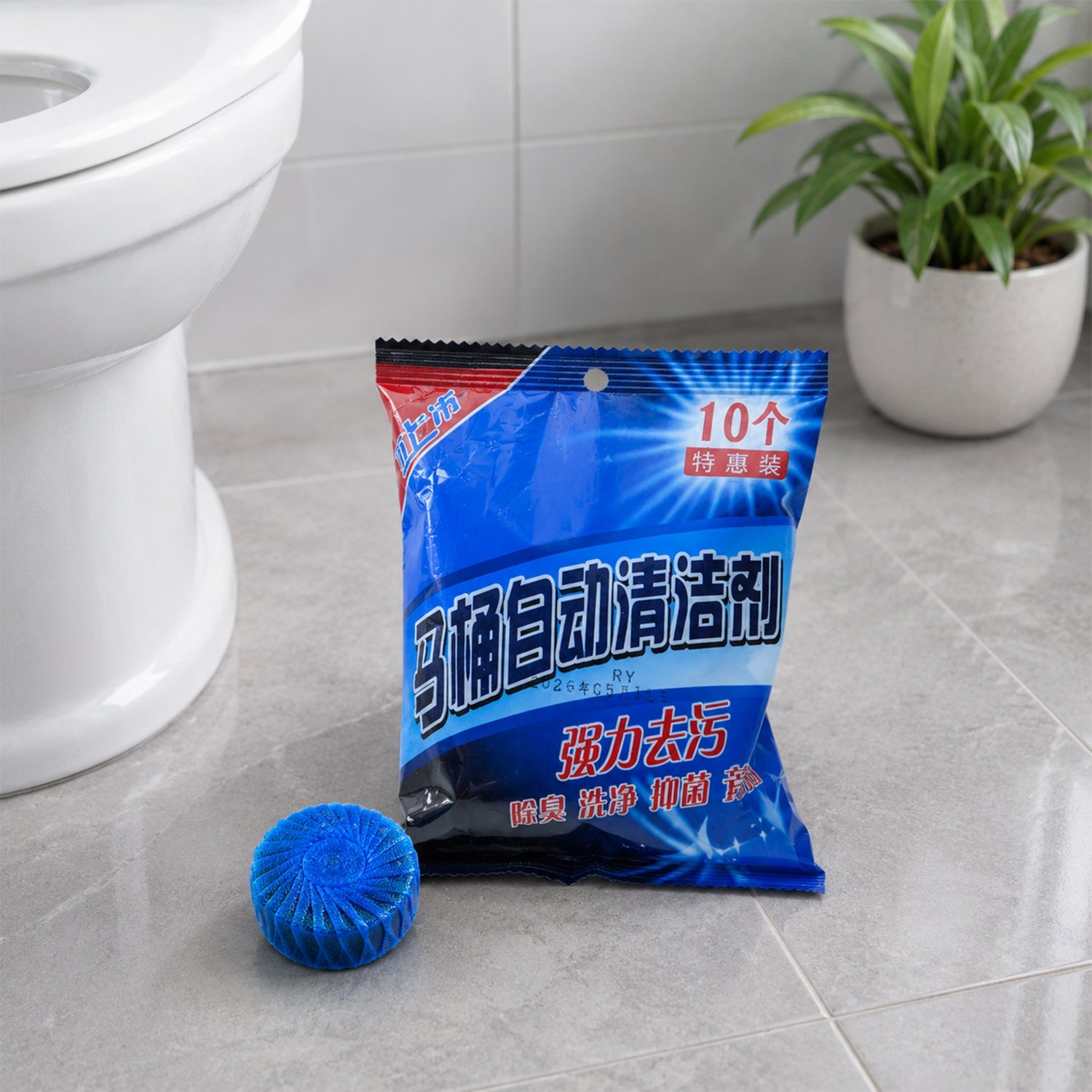 A blue toilet cleaner tablet rests next to its blue and black packaging on a tiled bathroom floor.