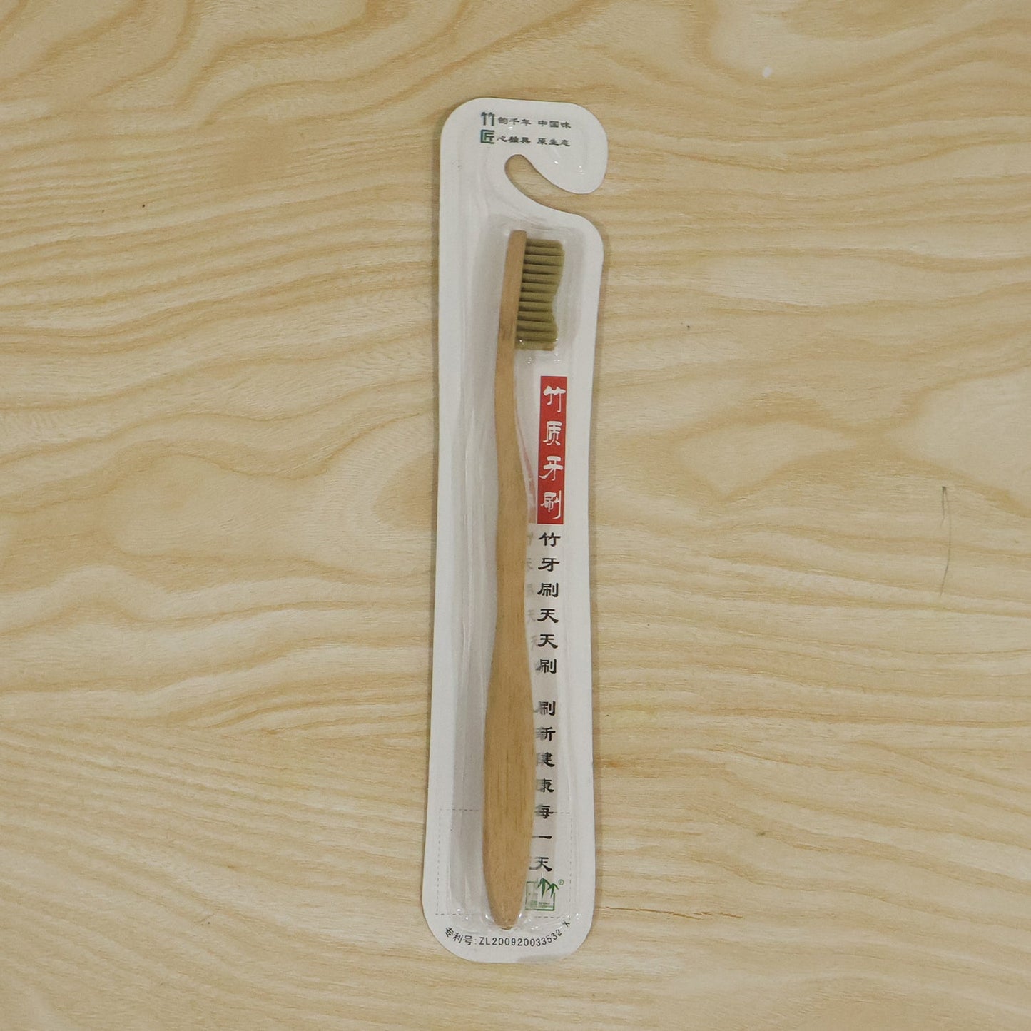 A bamboo toothbrush in clear plastic packaging with Chinese text, laid on a light wooden surface.