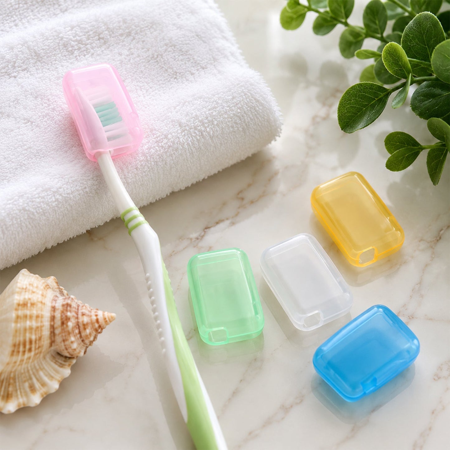 A pink toothbrush head cover protects a white toothbrush with green bristles on a white marble surface with a seashell.
