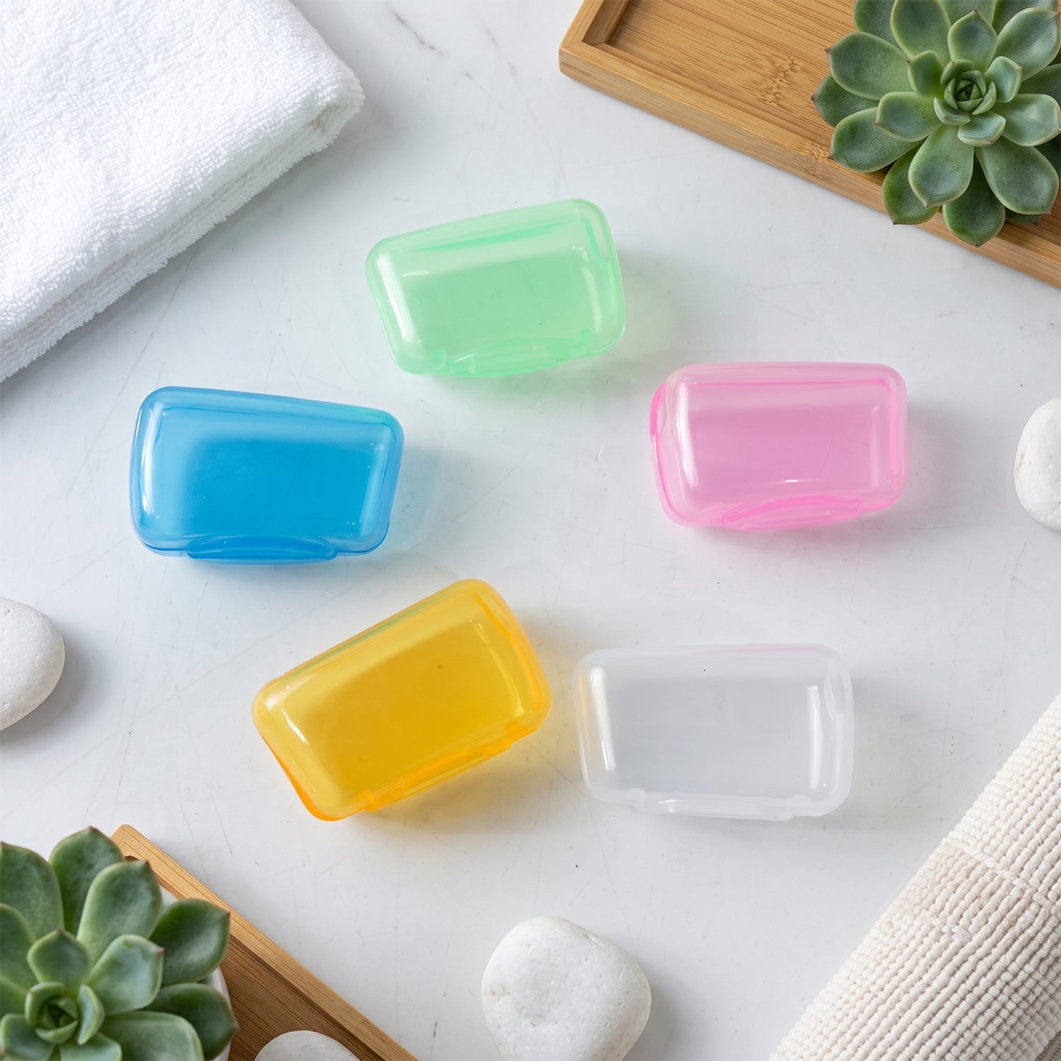 Five translucent toothbrush head covers in blue, green, pink, yellow, and clear are scattered on a white marble surface.