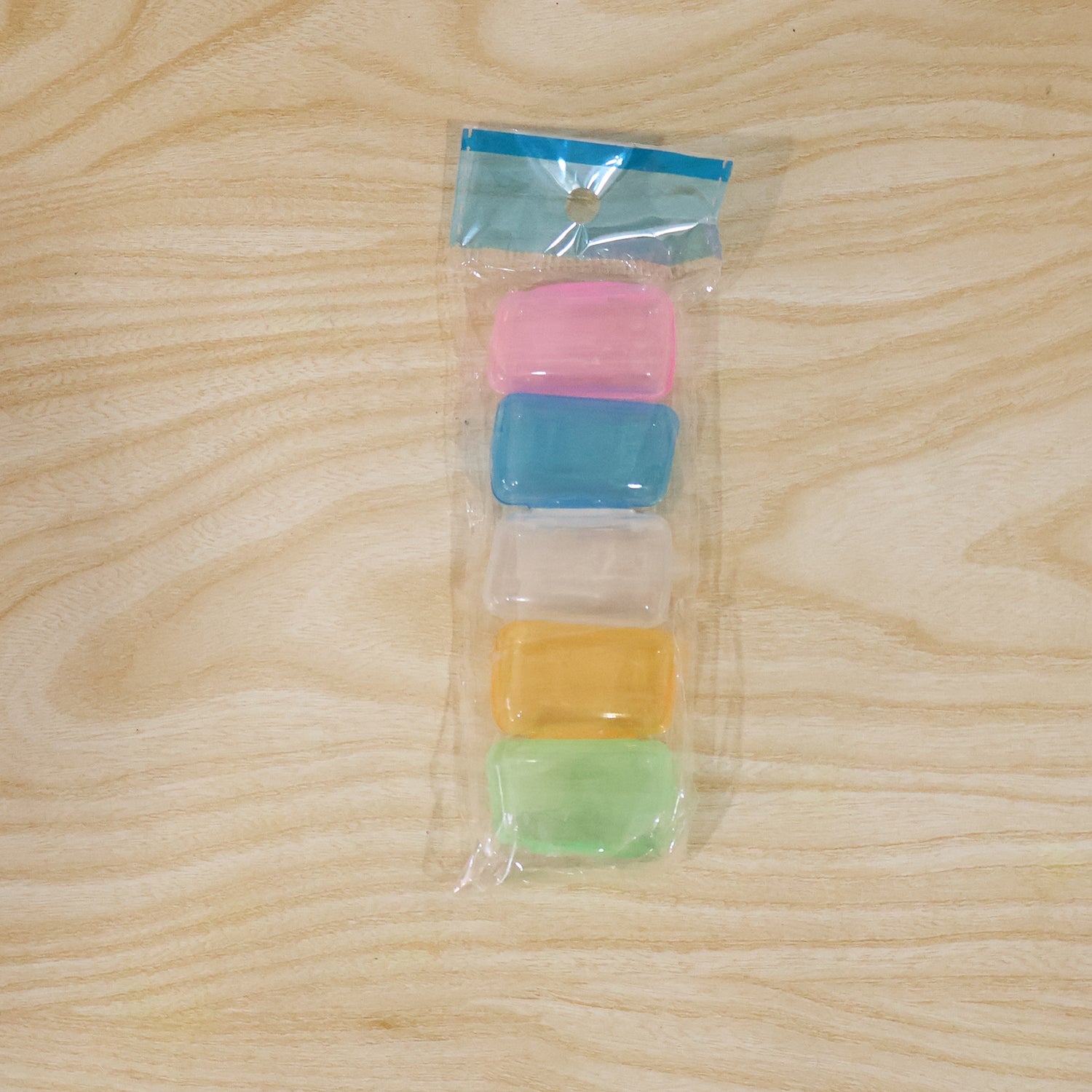 A clear plastic package contains five stacked translucent toothbrush head covers in pink, blue, clear, yellow, and green.