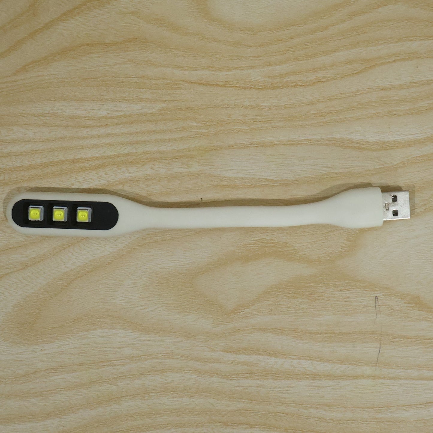 A white flexible USB LED light with three yellow LED bulbs and a USB-A connector resting on a light wood grain surface.