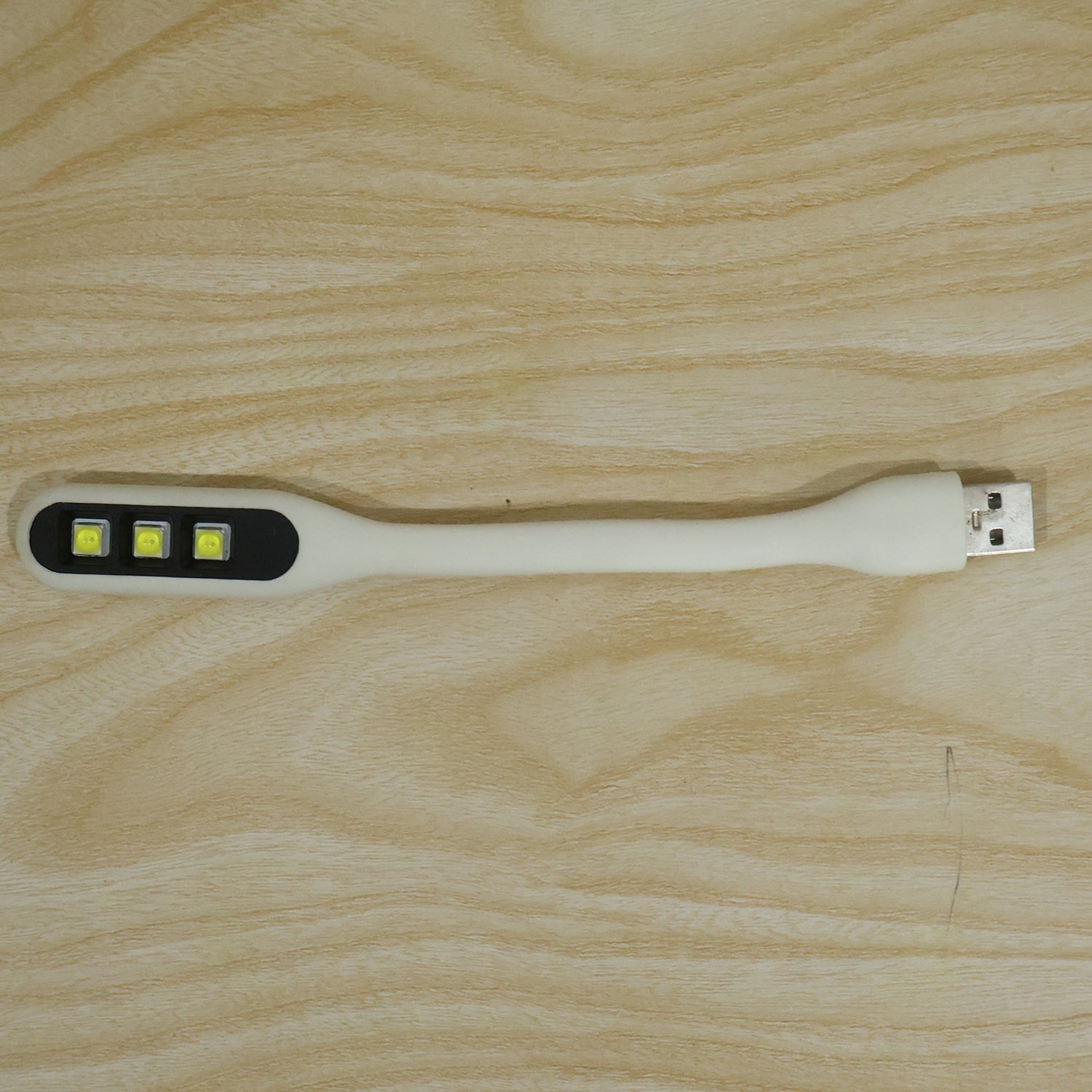 A white flexible USB LED light with three yellow LED bulbs and a USB-A connector resting on a light wood grain surface.