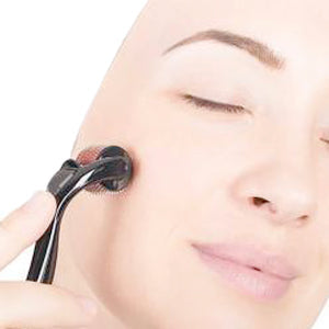 A woman with closed eyes gently rolls a black derma roller across her cheek.