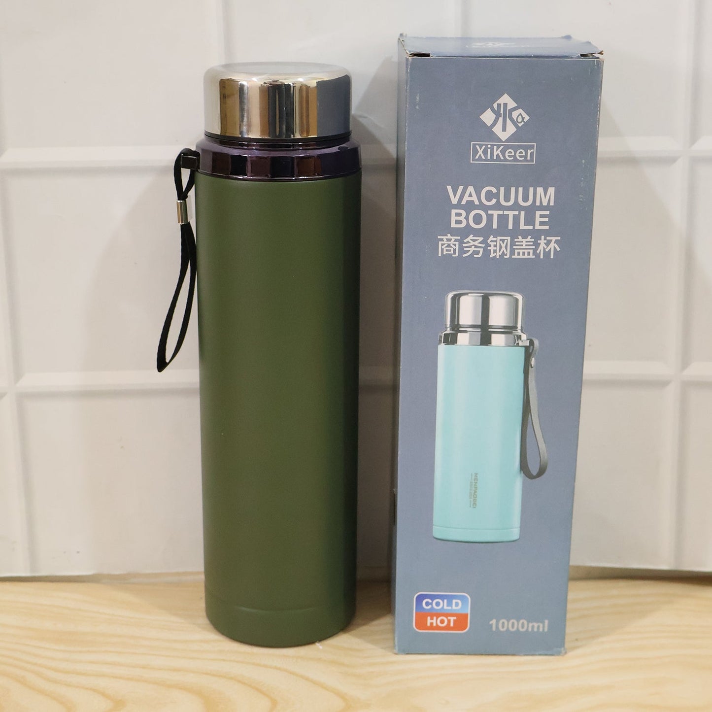 A matte green water bottle with its packaging box, which features a light blue bottle on the front, against a white tiled