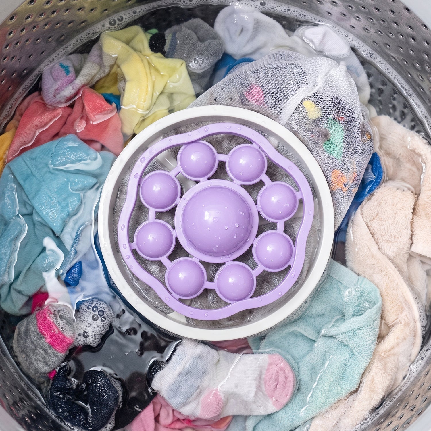 A purple and white floating lint mesh bag in a washing machine with various colorful clothes.