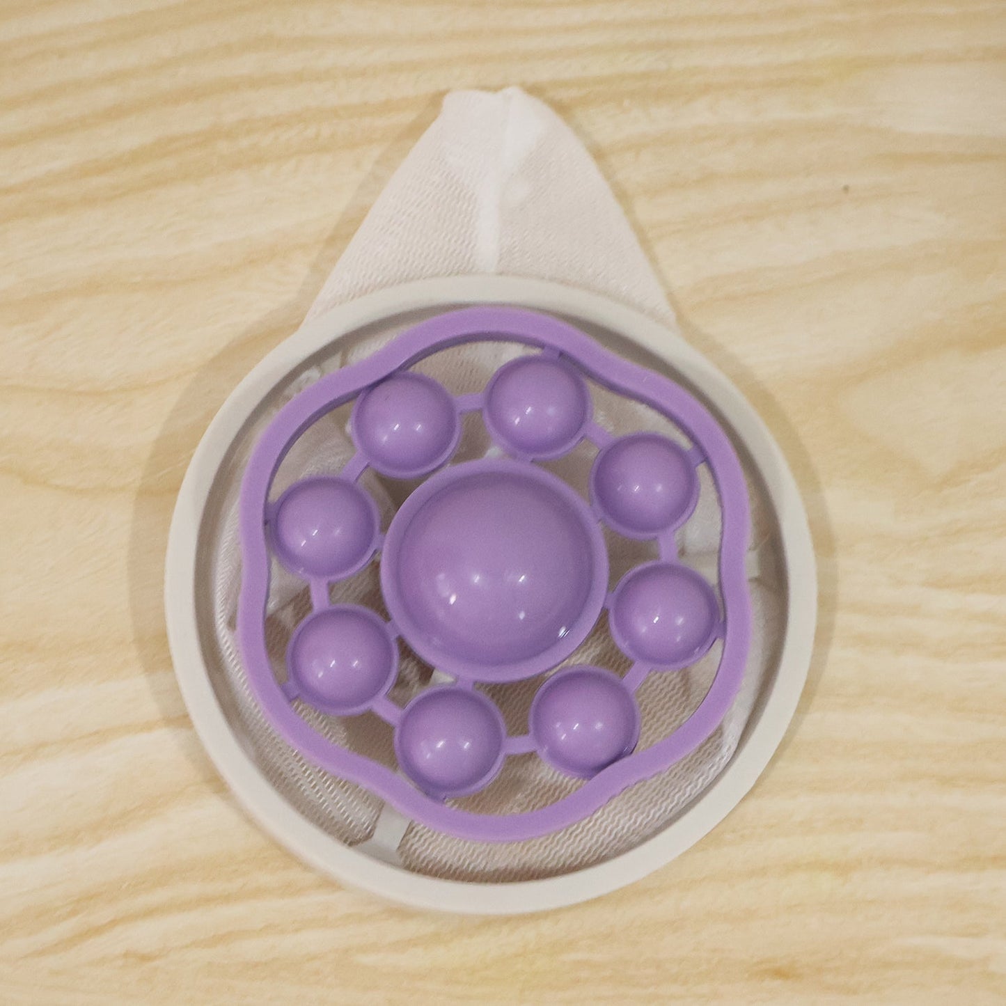 The top view of a purple and white floating lint mesh bag on a light wooden surface.
