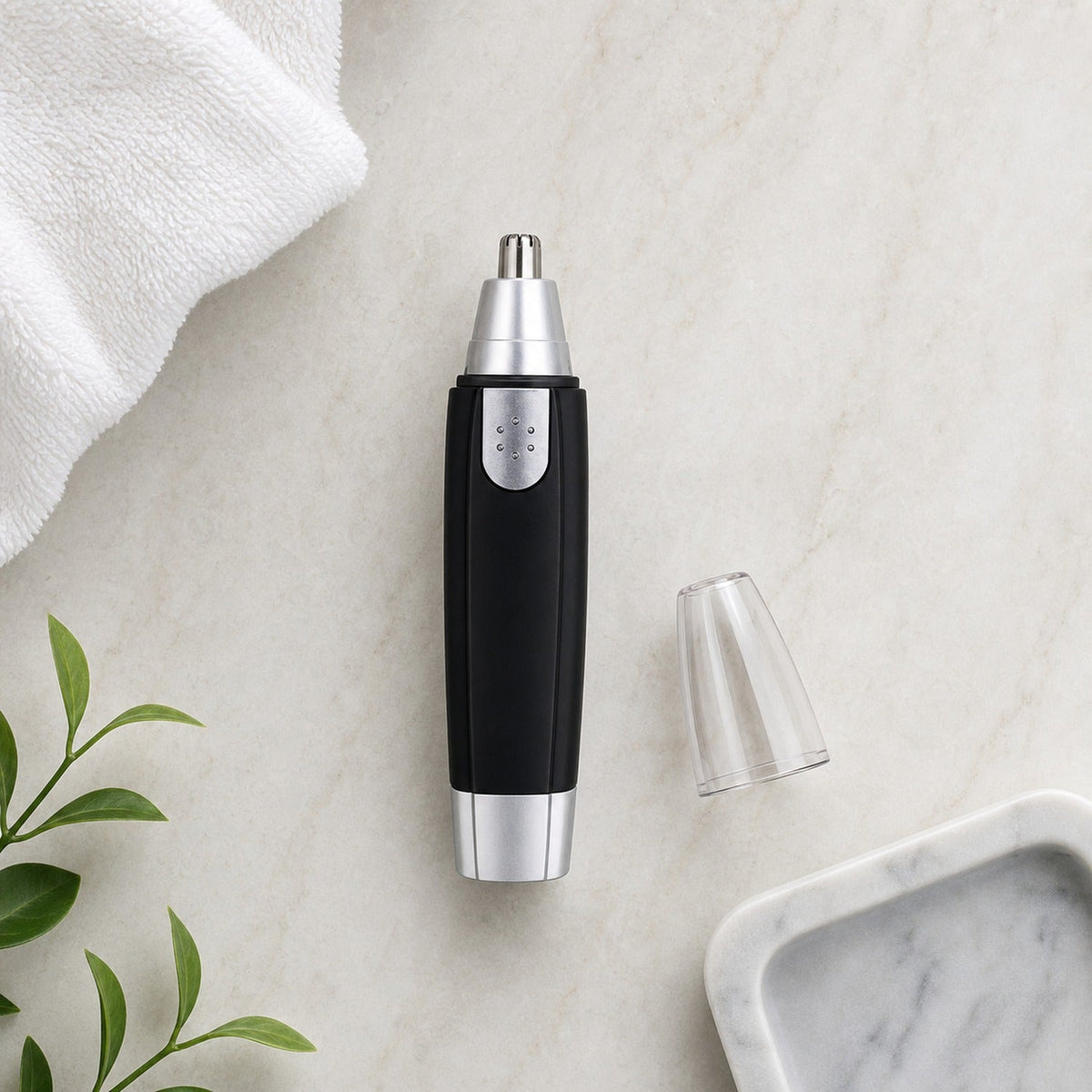 A black and silver nose hair trimmer with its clear cap removed lies on a white marble surface next to a white towel and