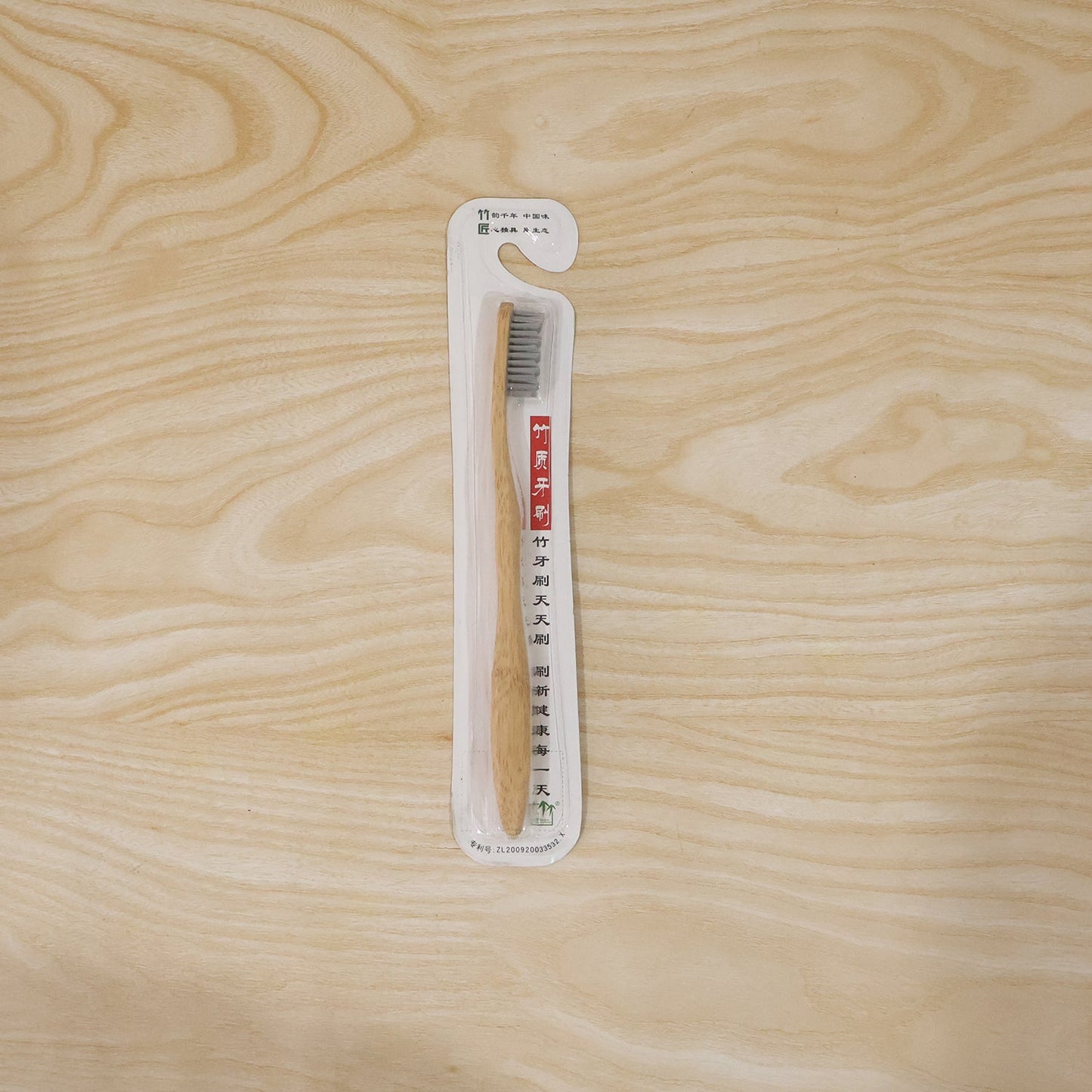 A single bamboo toothbrush with grey bristles is sealed in clear plastic packaging with Chinese text, lying on a light