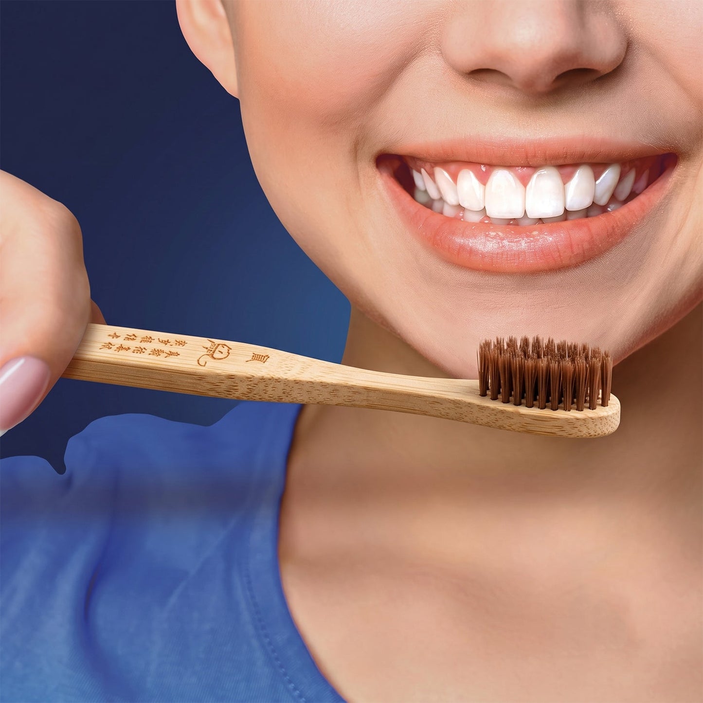 A person with a bright smile holds a bamboo toothbrush with brown bristles and an engraved handle near their mouth.