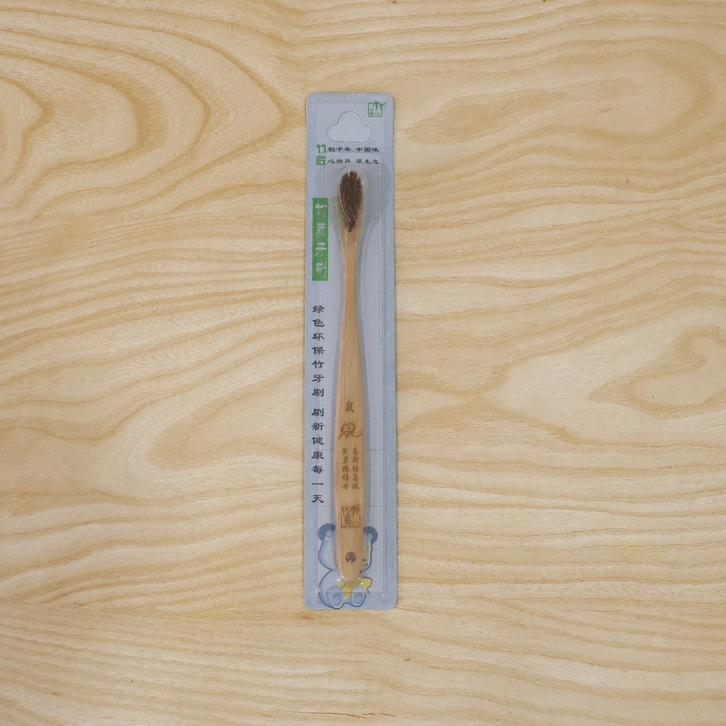 A bamboo toothbrush with brown bristles and an engraved handle is sealed in clear plastic packaging with green and blue