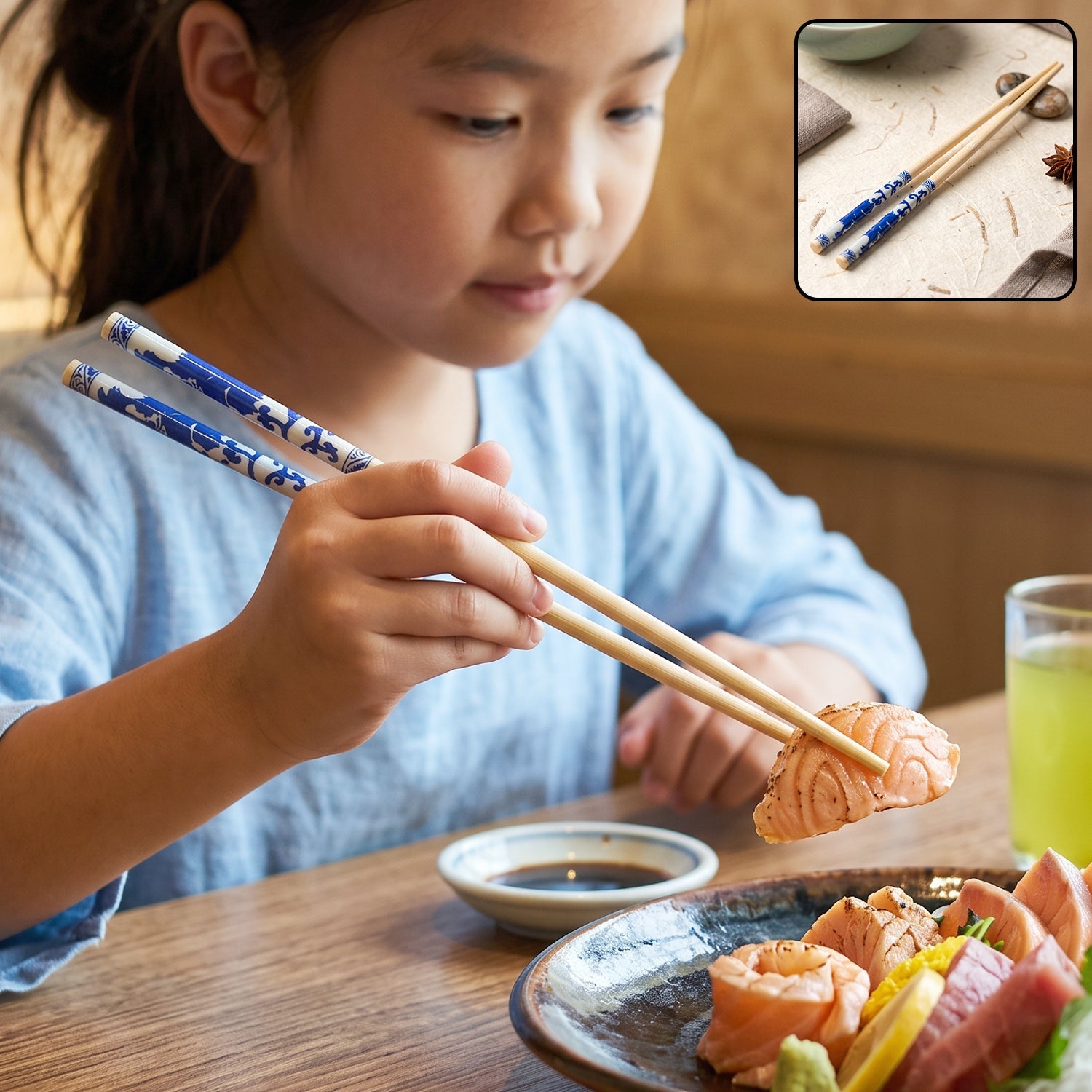 A young girl in a blue shirt uses bamboo chopsticks with blue Chinese print to pick up a piece of salmon.