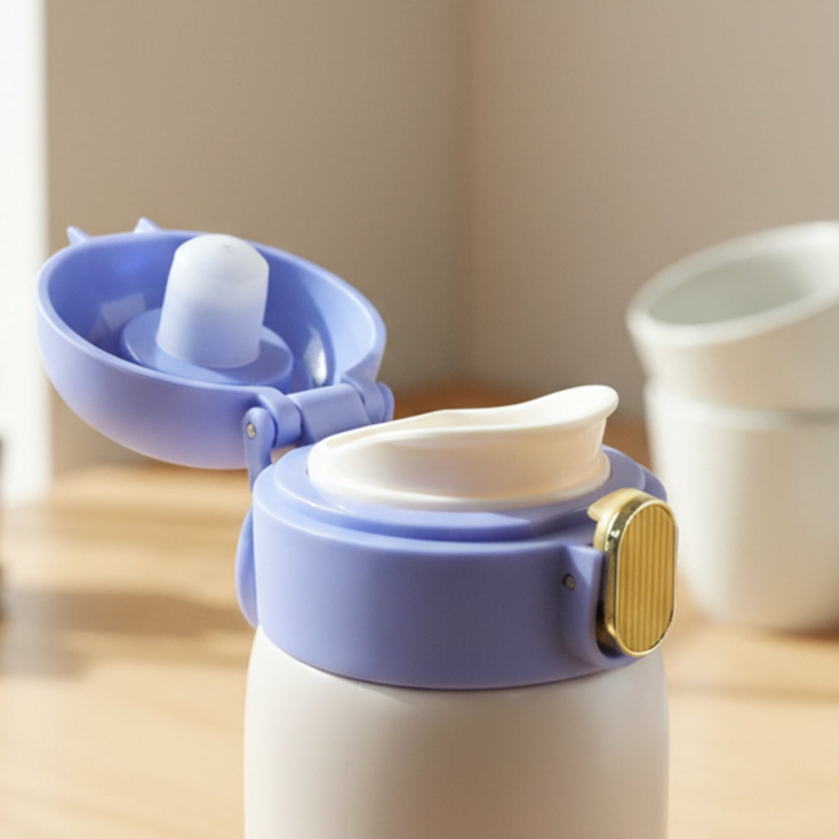 Close-up of the open blue lid of a water bottle, revealing the white drinking spout and gold latch.