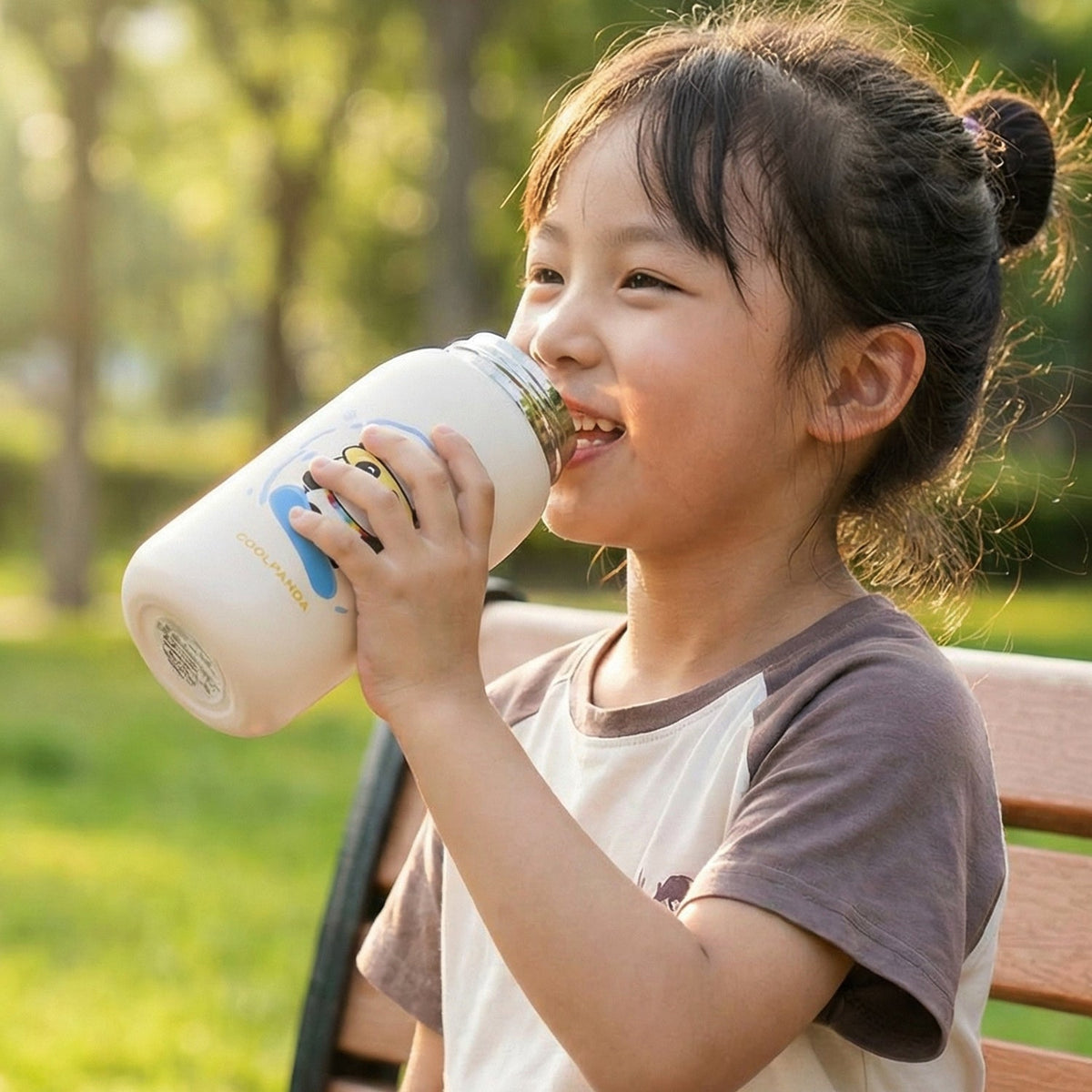A young girl with her hair tied back sips from a cream water bottle with a panda design.