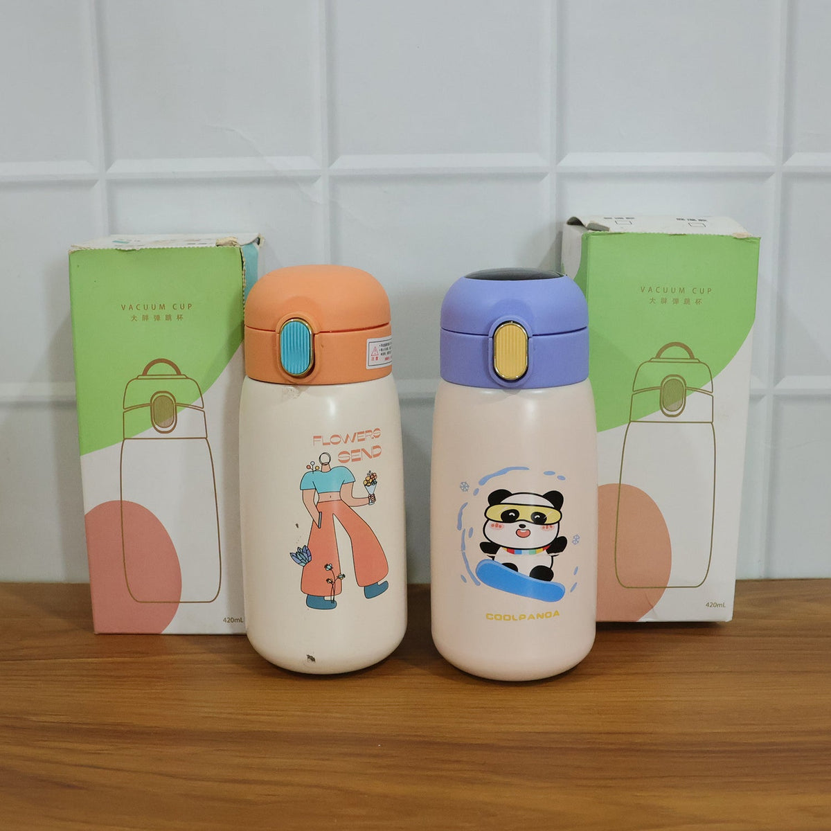 Two cream water bottles with cartoon designs stand in front of their green and white packaging boxes.