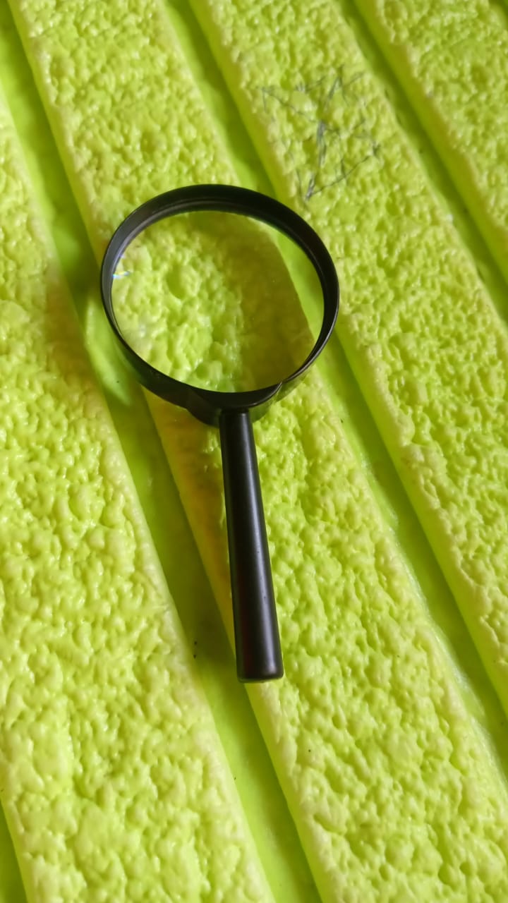 A black magnifying glass is placed on a textured, bright green surface with parallel ridges.