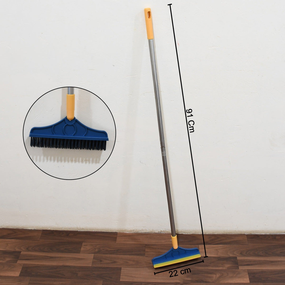 Blue and yellow floor cleaning brush with dimensions of 91 cm length and 22 cm width, shown against a white wall and wooden