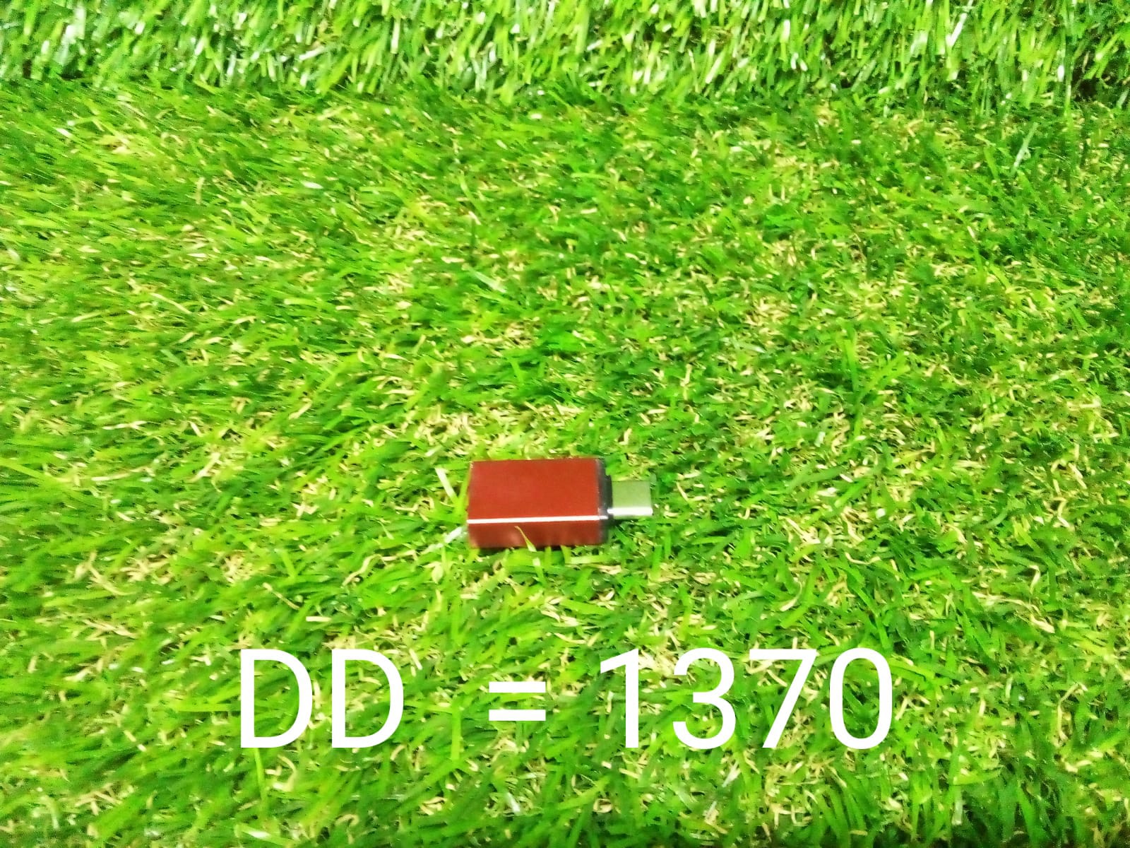 A small red USB-C to USB 3.0 OTG adapter is centered on a vibrant green artificial grass background.