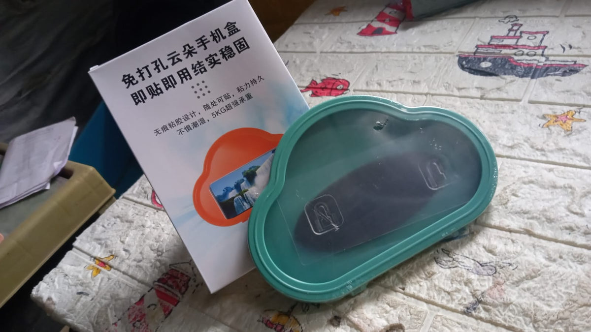 A teal cloud-shaped phone holder and its white instruction manual on a textured surface.
