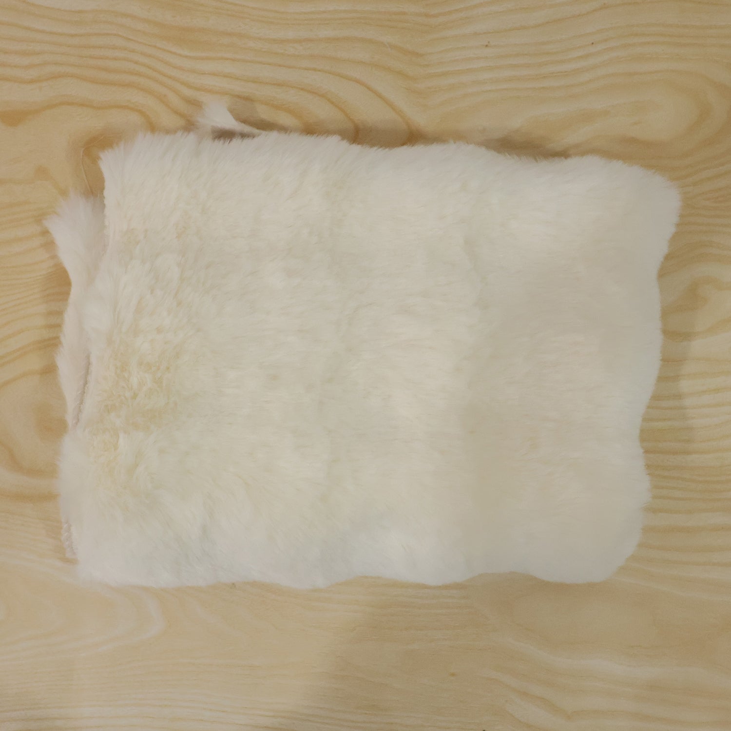 A folded cream fluffy faux fur rug swatch on a light wooden surface.