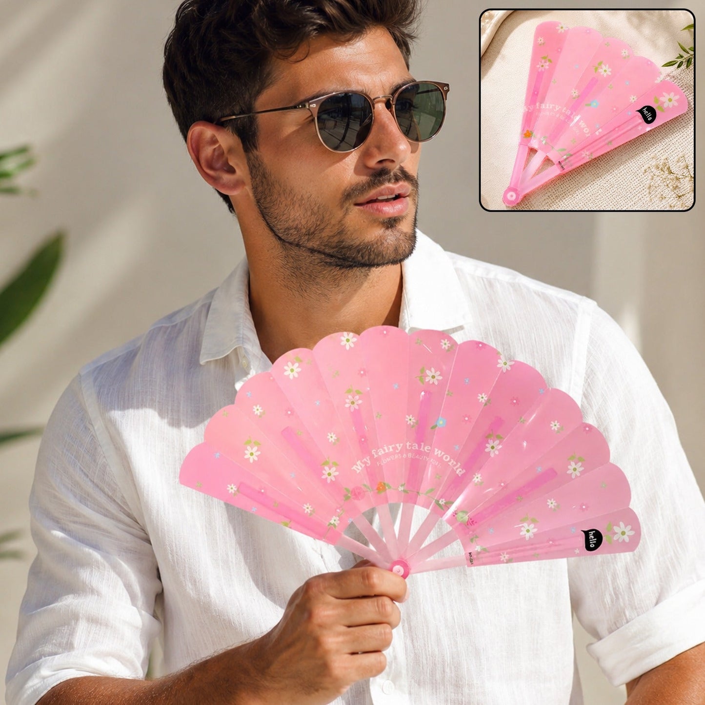A man in sunglasses and a white shirt holds an open pink fan with white flowers and text; a smaller inset shows the fan