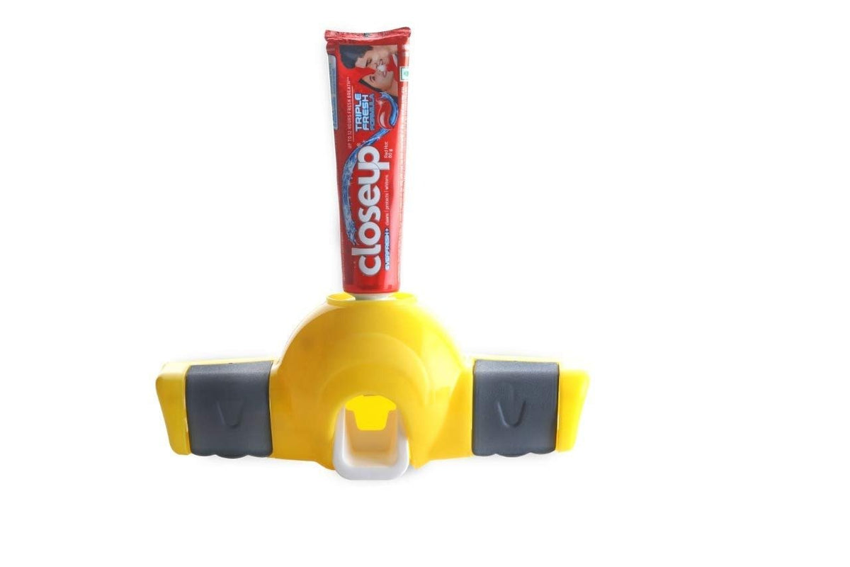 Yellow and gray toothpaste dispenser with a red toothpaste tube inserted, isolated on a white background.