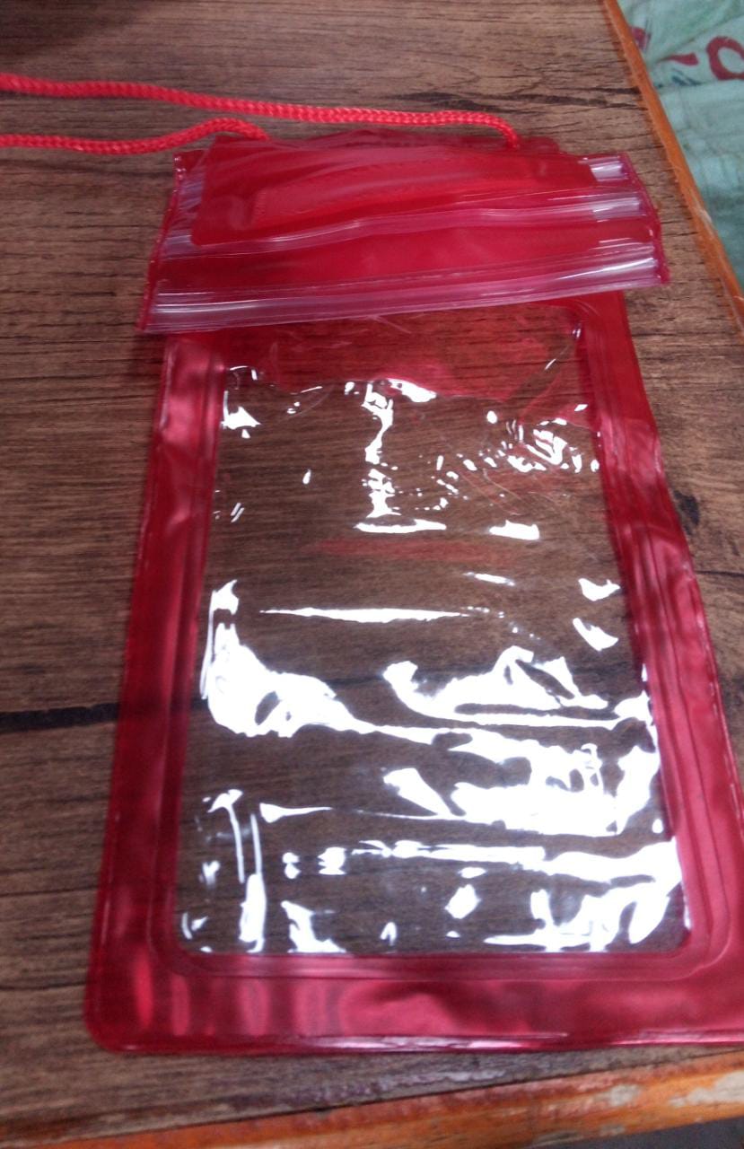 A transparent red waterproof mobile pouch with a clear window and a matching red lanyard is laid flat on a wooden surface.