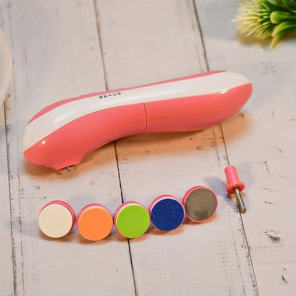 A pink and white electric nail trimmer with five colorful grinding heads and a cylindrical head on a wooden surface.