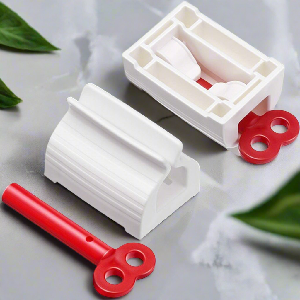 Two white plastic tube squeezers and a detached red winding key are displayed on a grey surface with green leaves.