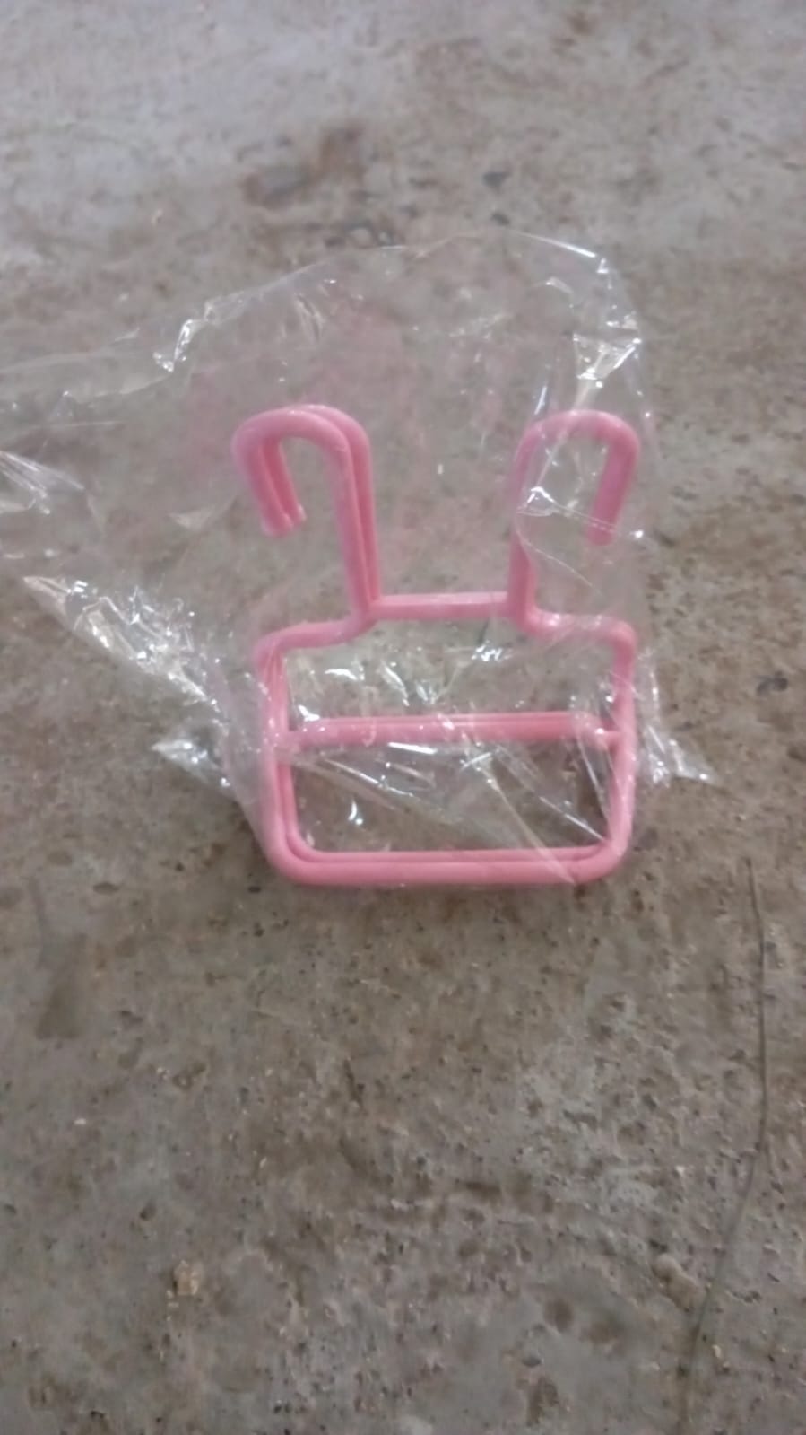 A single pink plastic shoe drying rack is inside a clear plastic bag on a grey concrete surface.