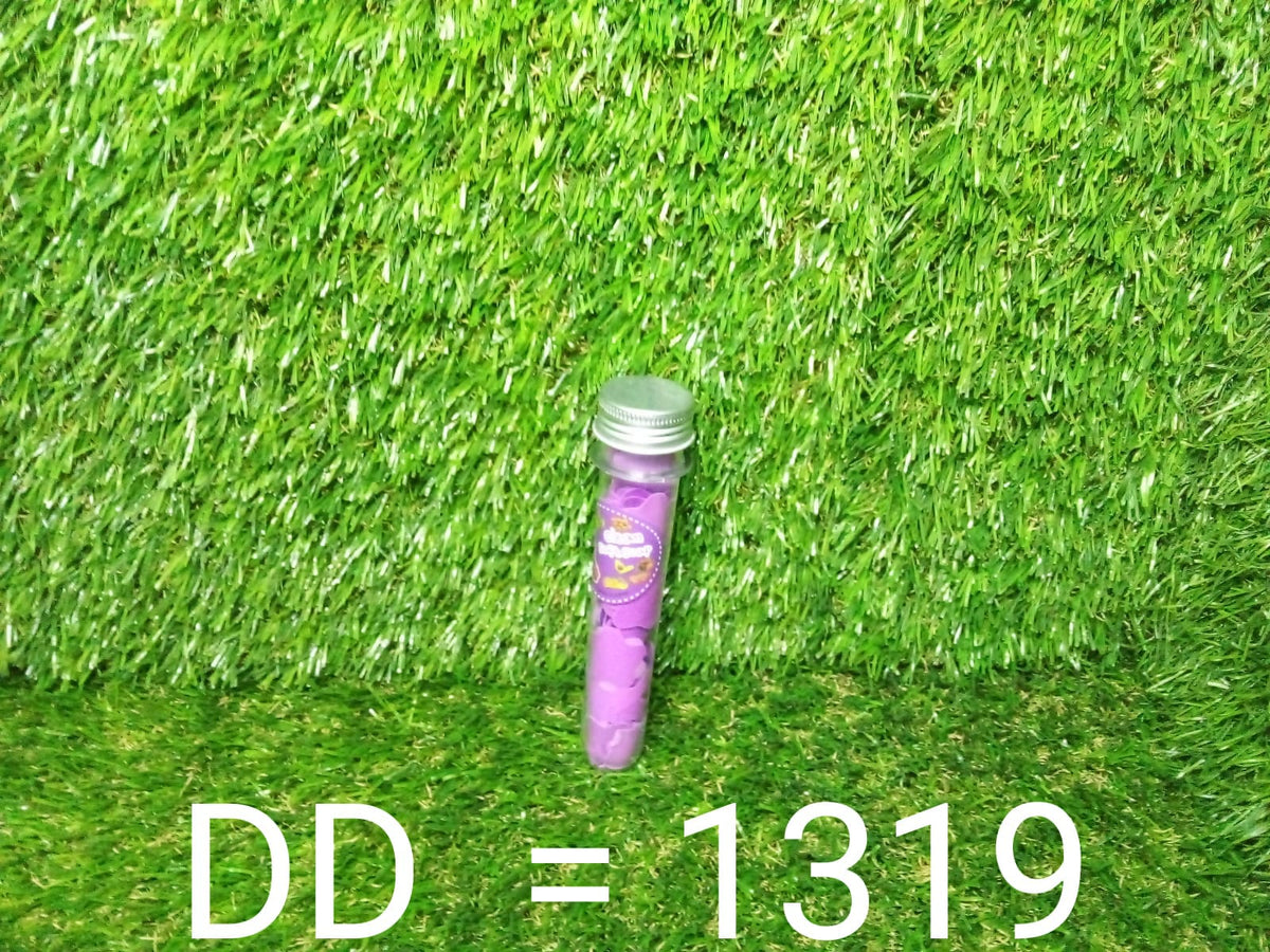 A clear tube with a silver cap and a purple label containing purple paper soap strips stands upright on a green artificial