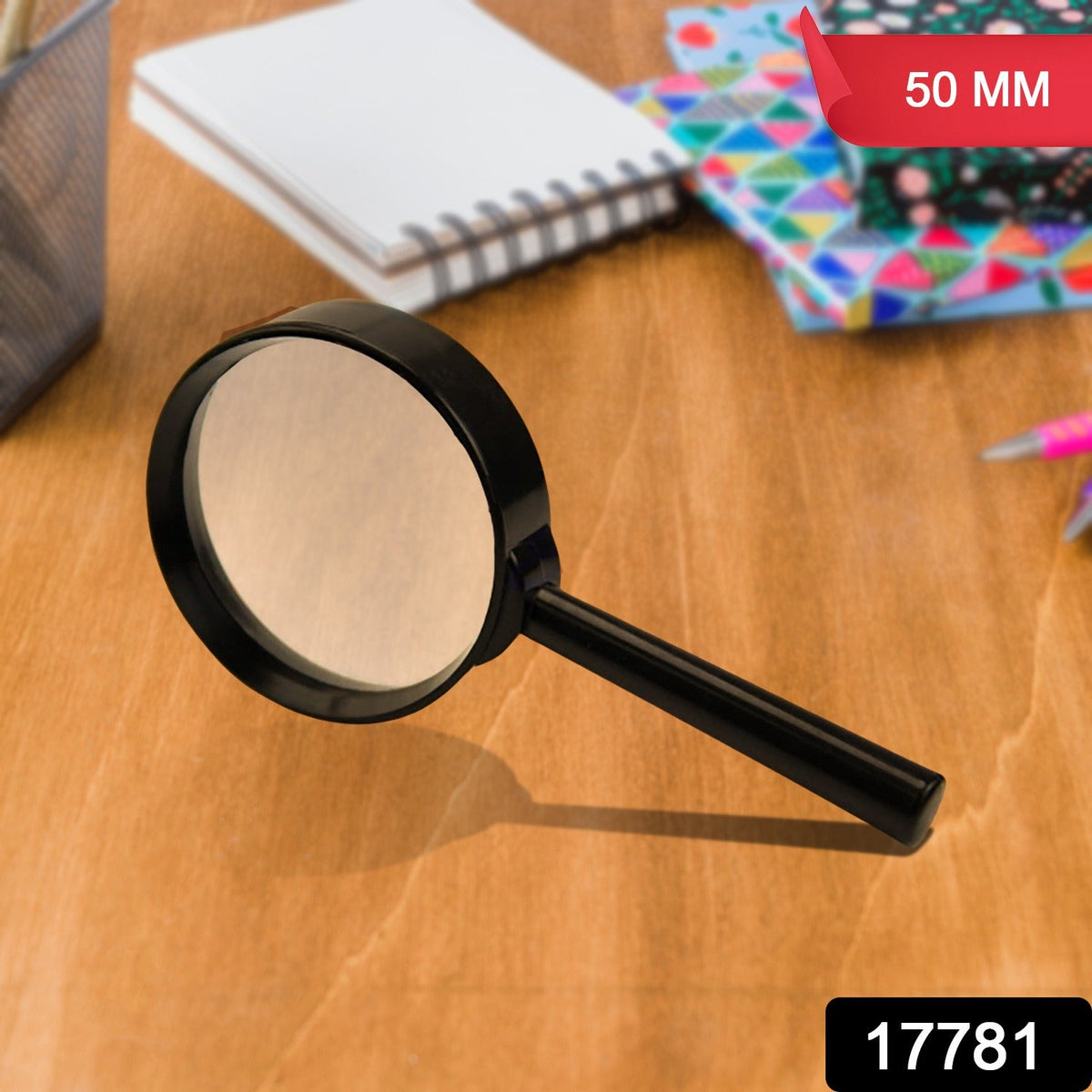 A black magnifying glass with a 50mm lens sits on a wooden desk with notebooks in the background.