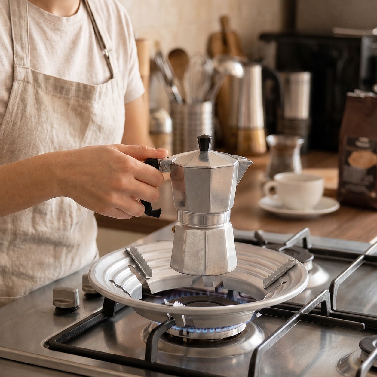 A person places a silver Moka pot onto the gas stove trivet over a lit burner.